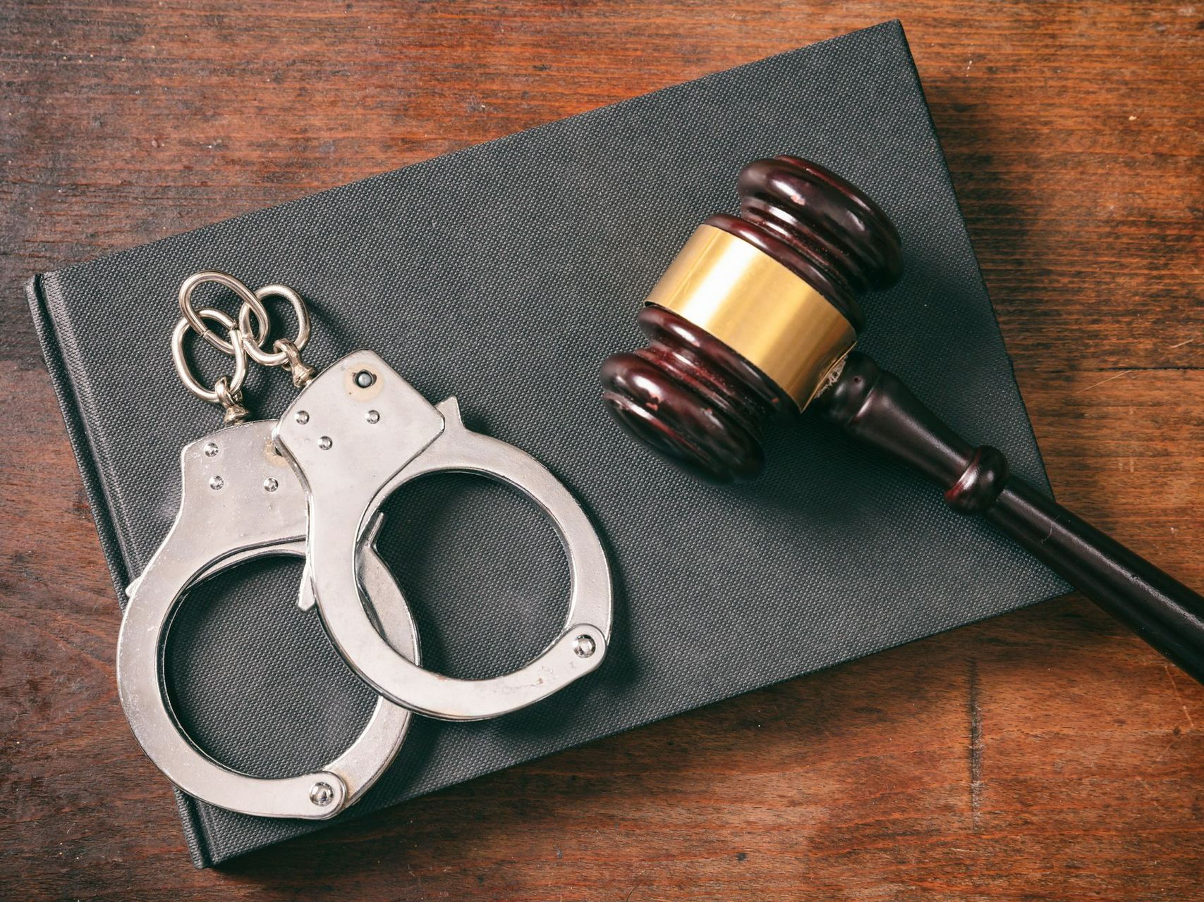 A pair of handcuffs and a judge 's gavel on top of a book.