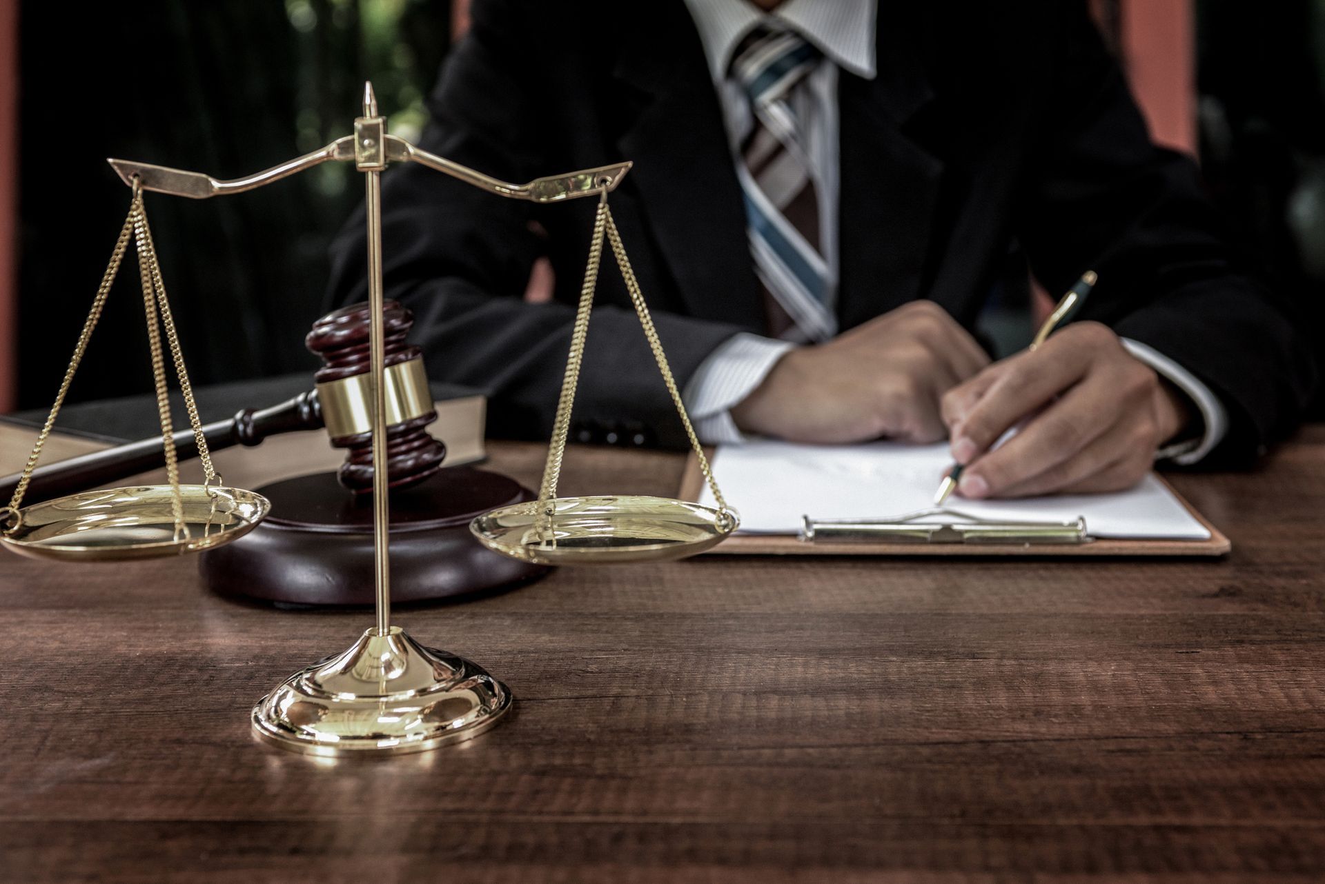 A man in a suit and tie is sitting at a table with scales of justice and a judge 's gavel.