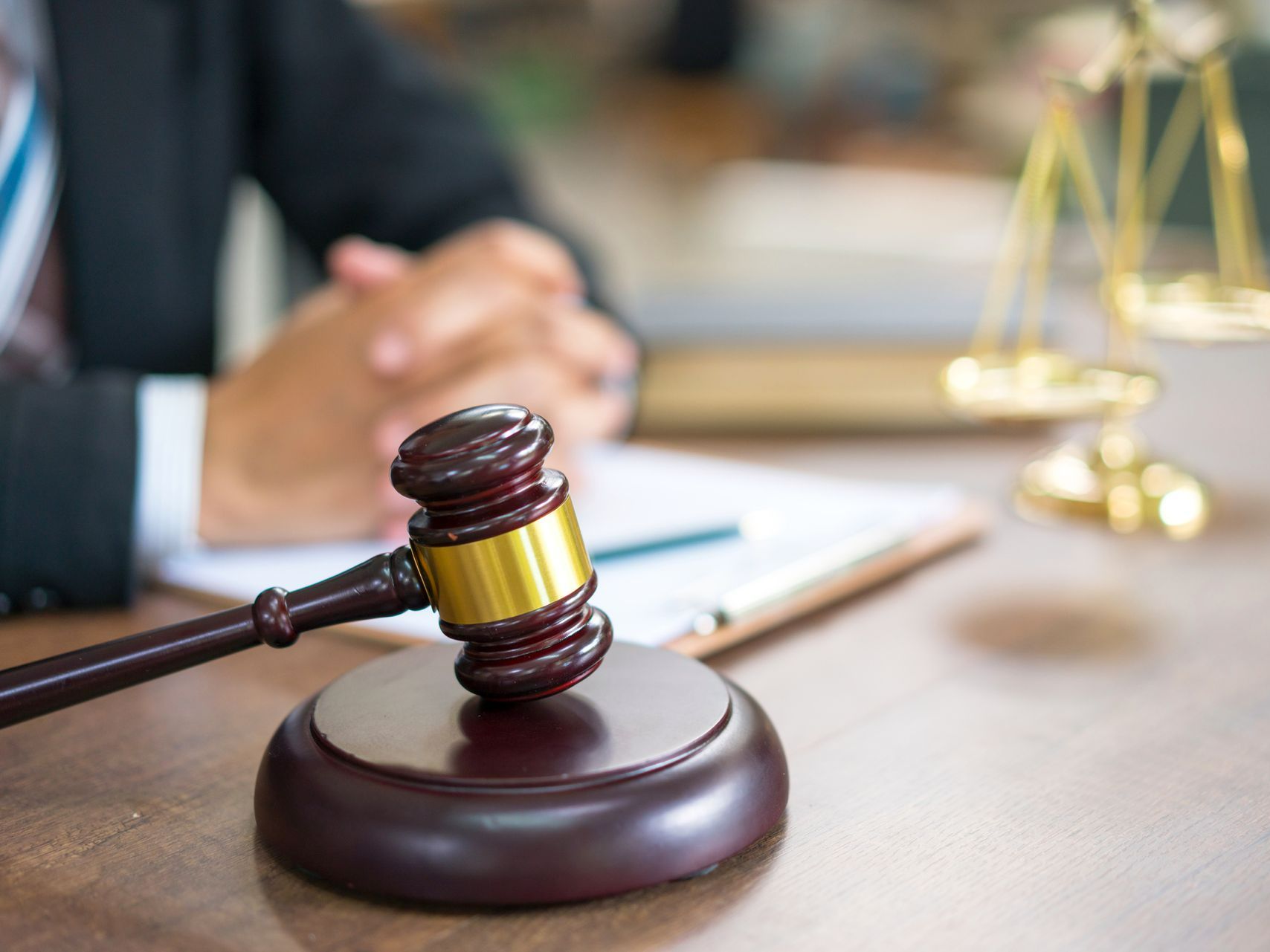 A judge 's gavel is sitting on a wooden table next to a scale of justice.