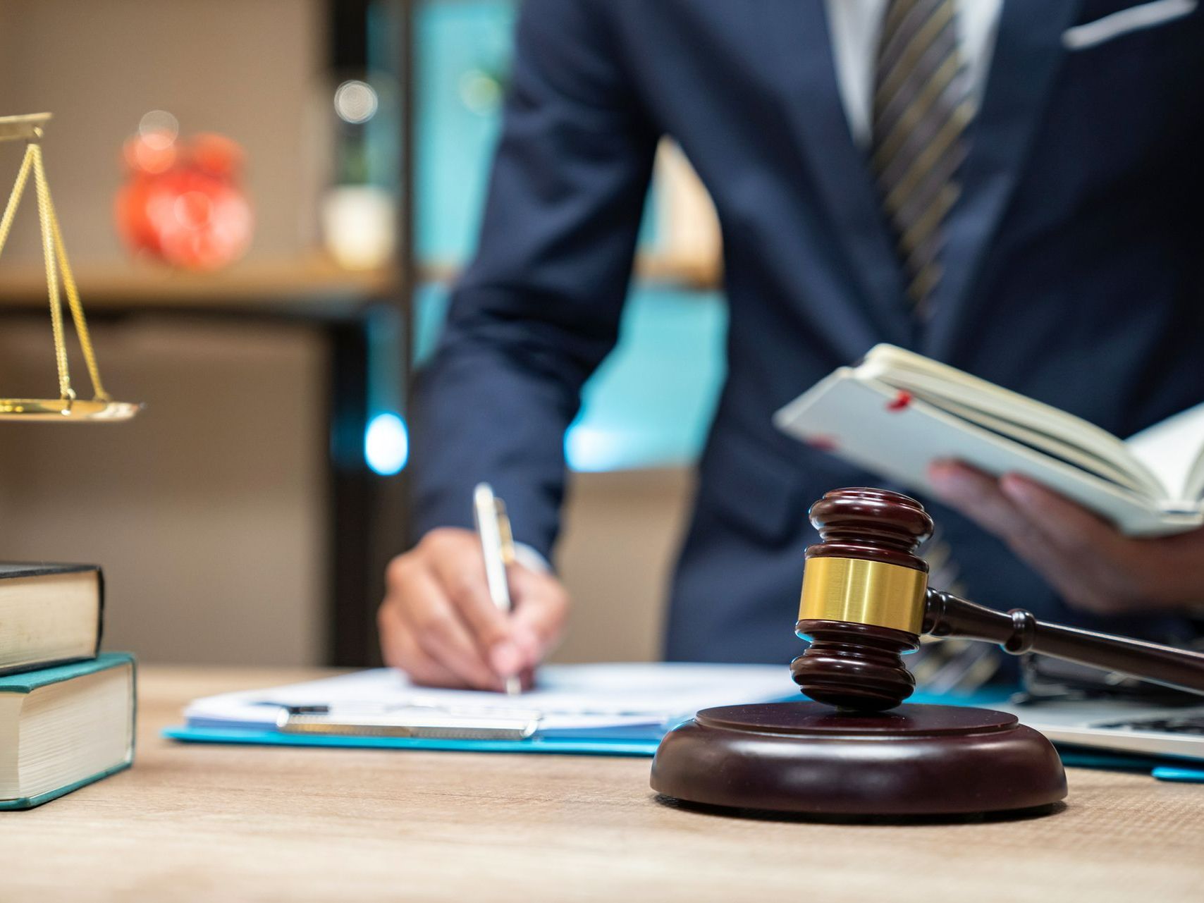 A man in a suit is writing on a clipboard next to a judge 's gavel.