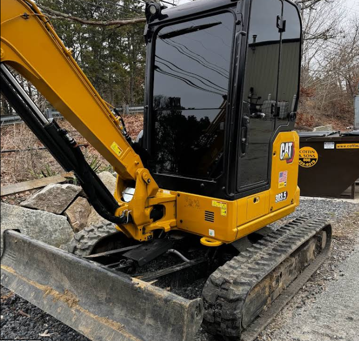 A yellow cat excavator is parked next to a dumpster