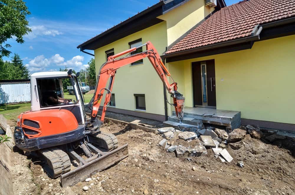 A Small Excavator is Sitting in Front of a Yellow House — Matt's Mini Machines in Rosemount, QLD