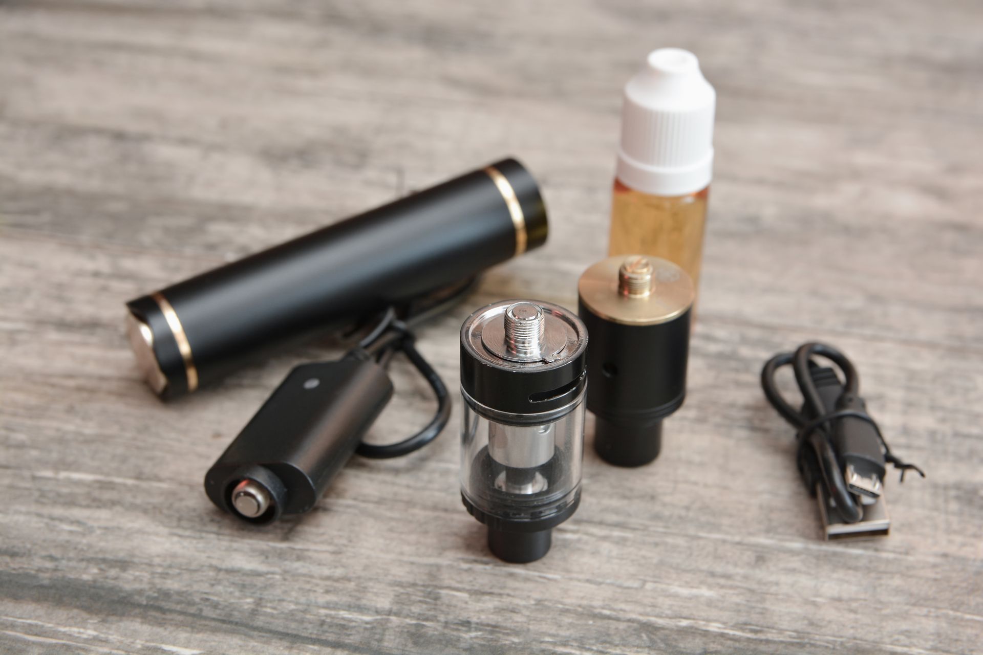 Penna per svapare nera e oro con accessori, tra cui un caricabatterie, un serbatoio e una boccetta di e-liquid, su legno.