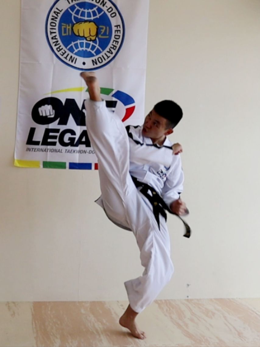 Martial artist in white uniform performing a high kick in front of a martial arts banner