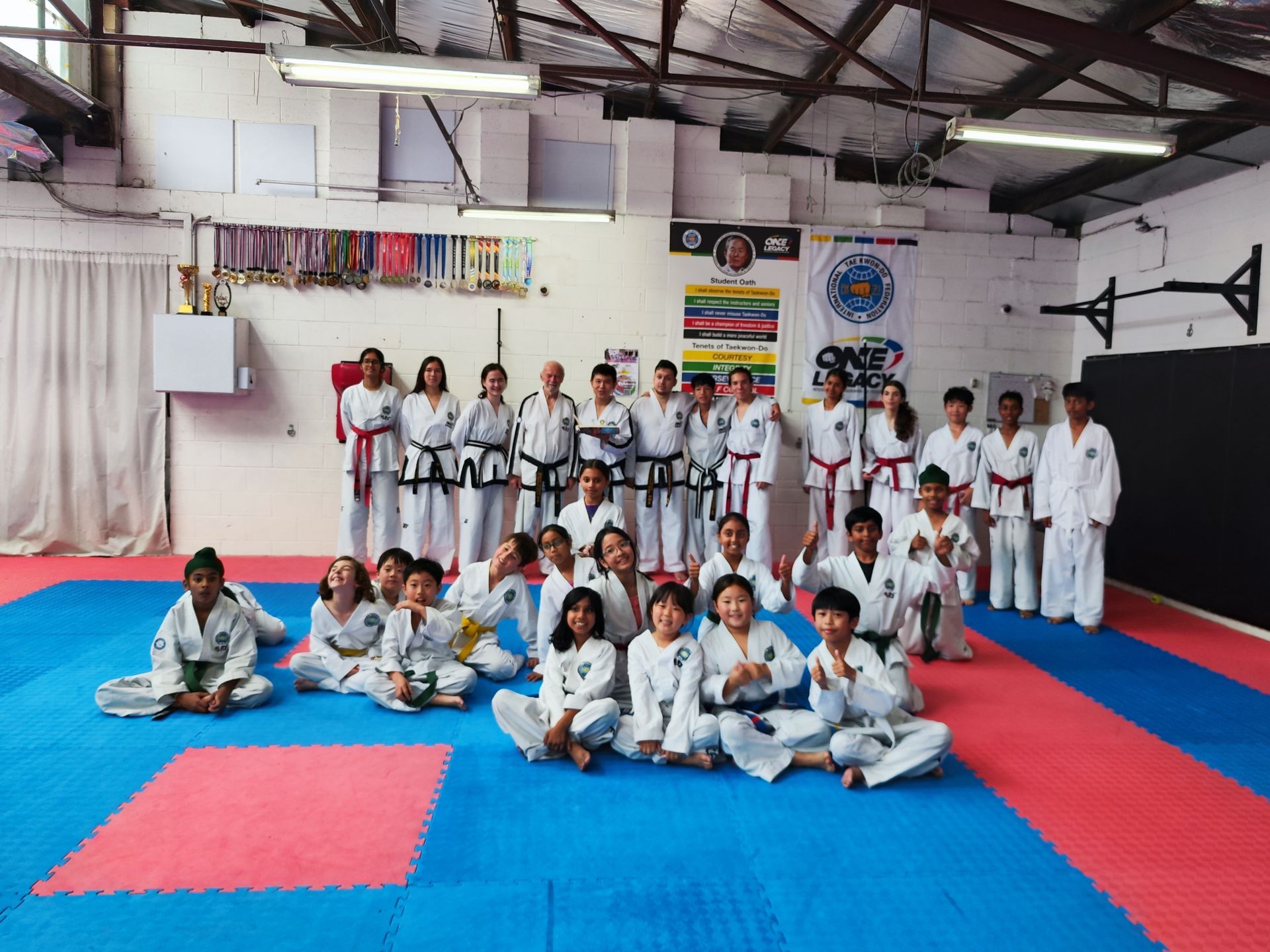 Martial arts class posing in white uniforms on blue and red mats inside a gymnasium