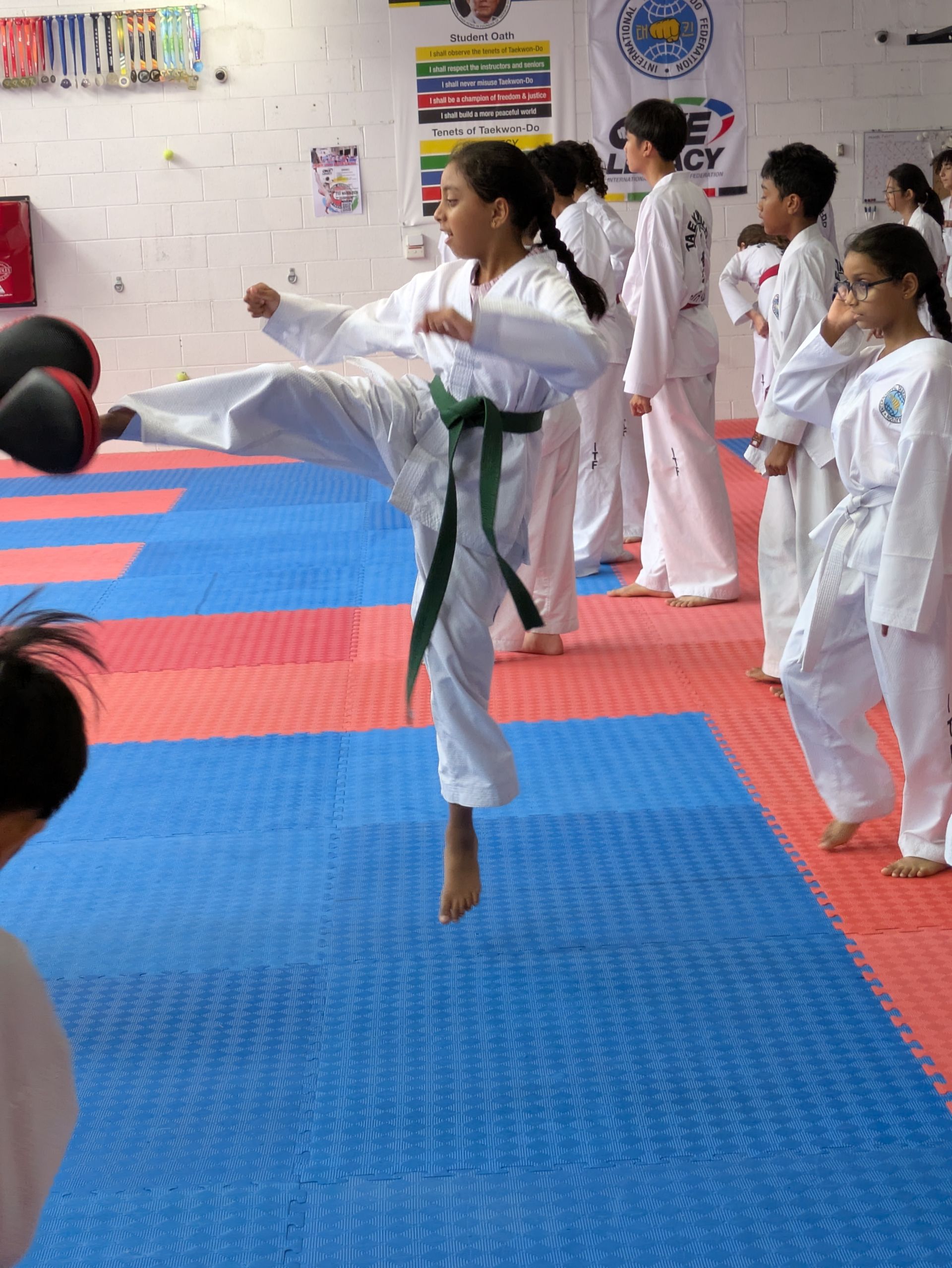 Martial arts class practicing kicks on blue and red mats in a training studio