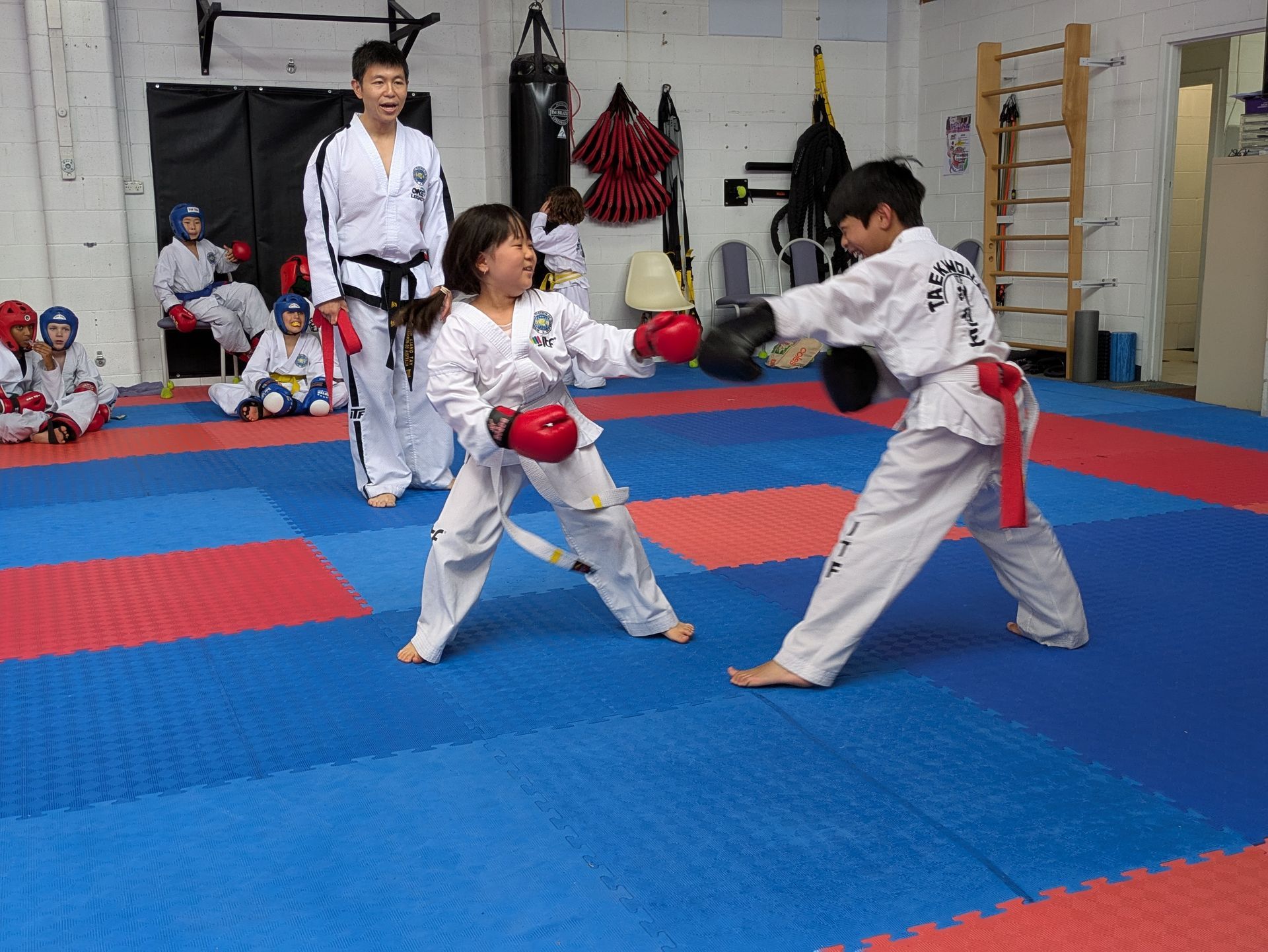 Martial arts class with two students sparring on blue mats while an instructor watches nearby