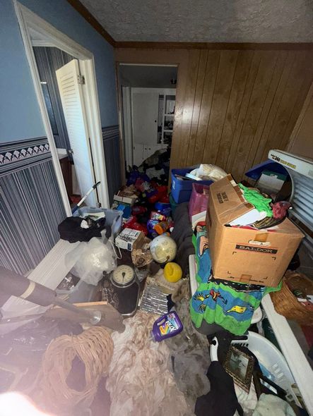 A cluttered room filled with boxes, various household items, and debris scattered across the floor and furniture.