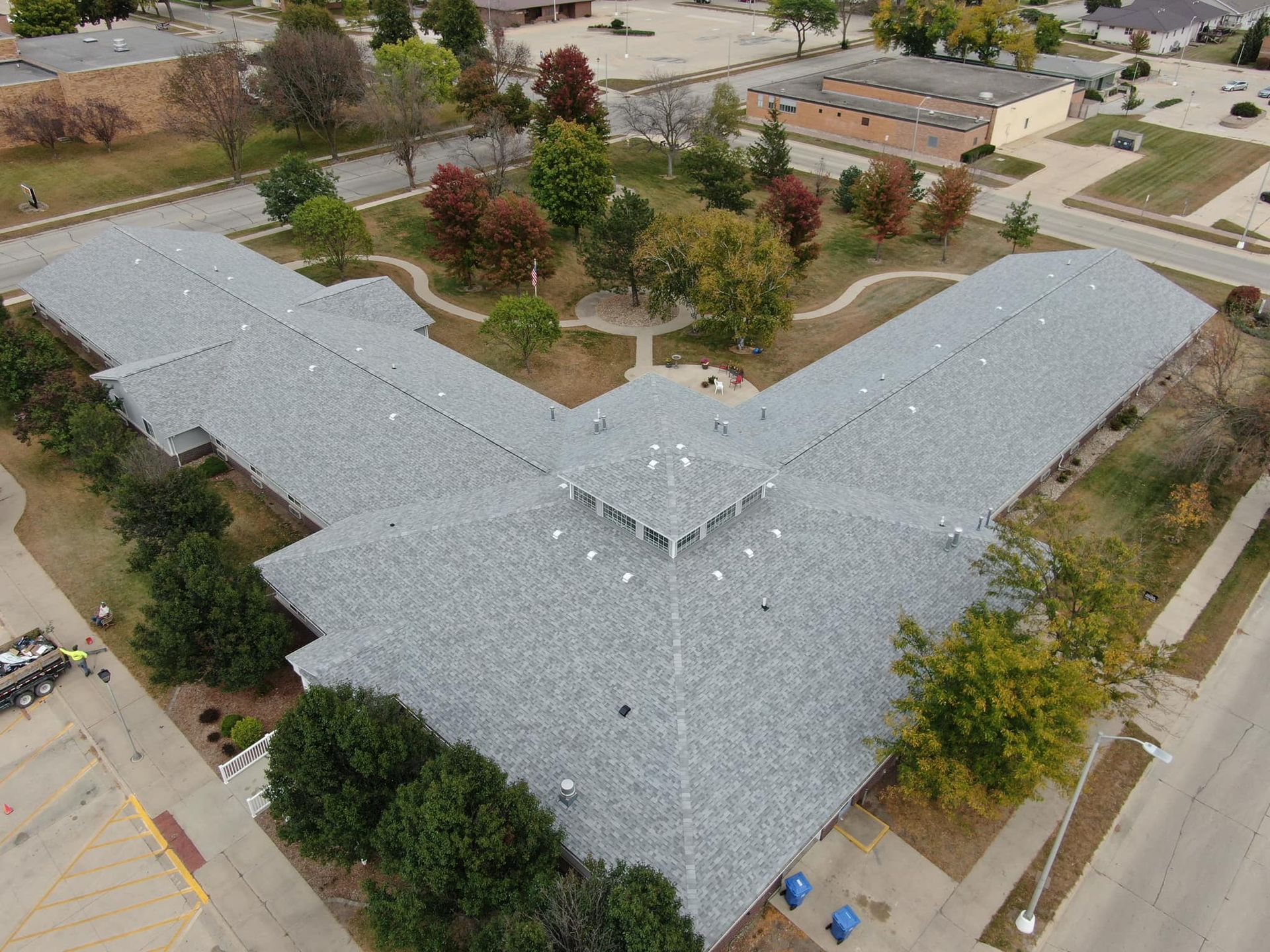 An aerial view of a large building with a gray roof surrounded by trees.