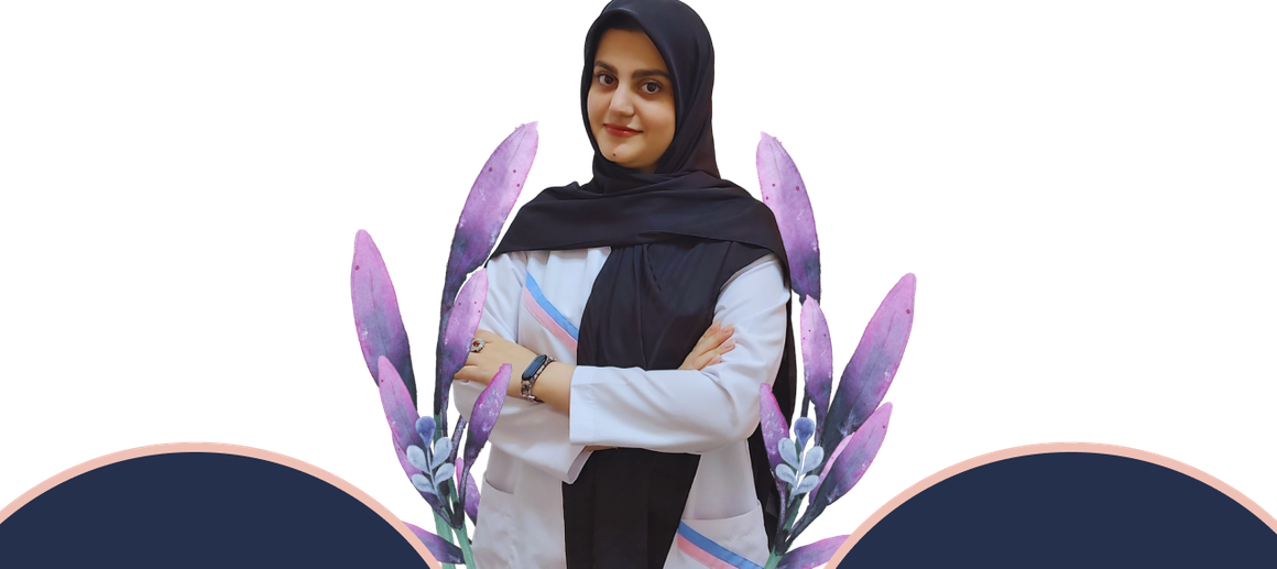 A woman in a hijab is standing with her arms crossed in front of purple flowers.Tuqa picture