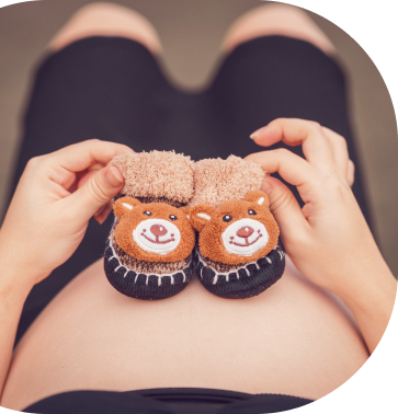 A pregnant woman is holding a pair of teddy bear baby shoes on her belly