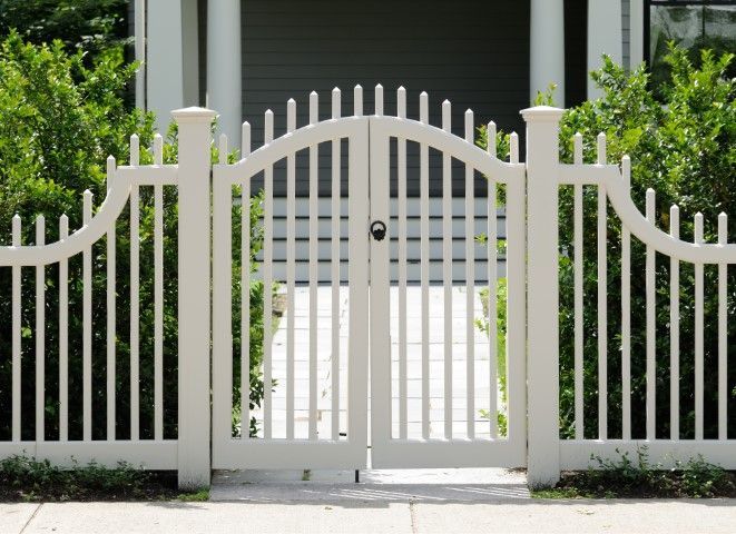 White picket fence with arched gate; view to a house entrance.