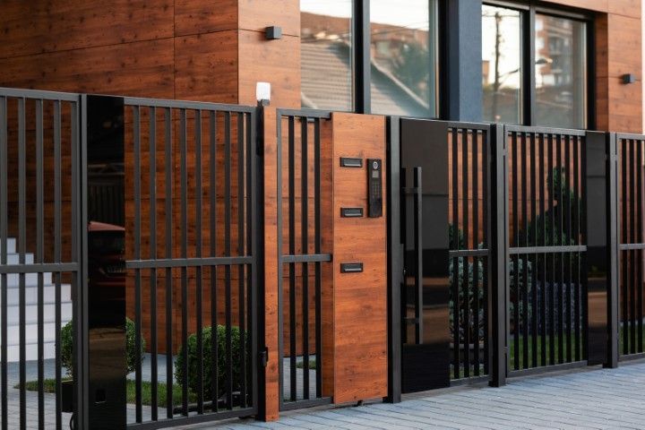Black metal and wood fence with a gate in front of a modern house.