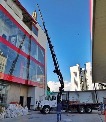 A white crane truck parked near a modern building with red and glass panels, extending its boom upward toward the roof.
