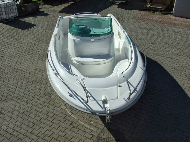 Een witte boot met een groene bovenkant staat geparkeerd op een bakstenen stoep