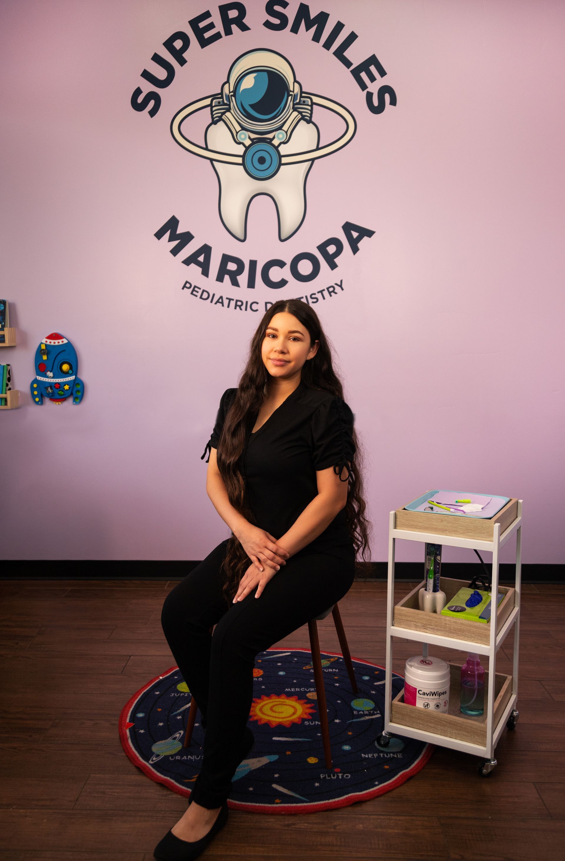A woman is sitting on a stool in front of a wall with a tooth on it.