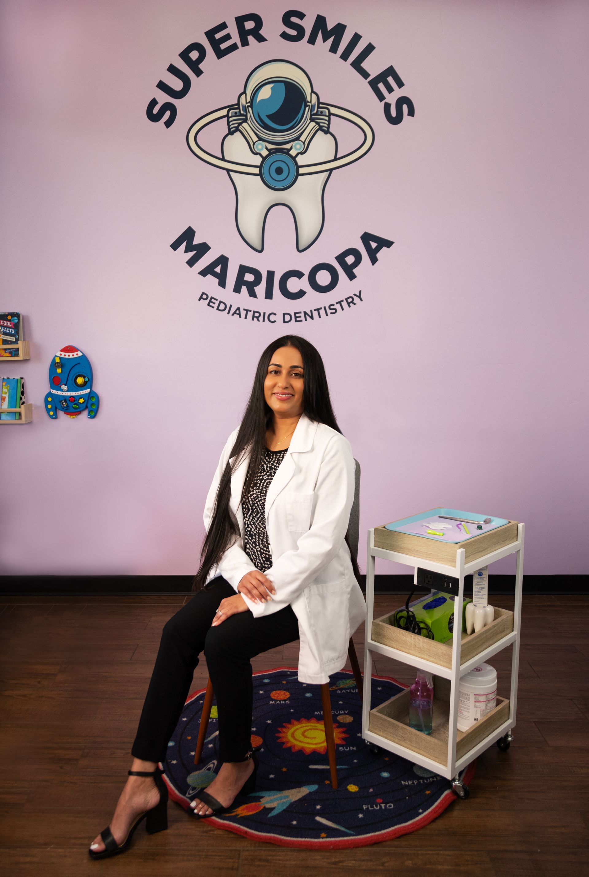 A female dentist is sitting in a chair in front of a wall with a tooth on it.