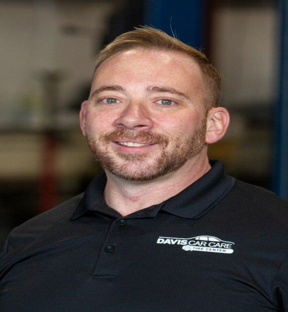 Smiling person in a black polo with a company logo, standing indoors against a blurred background