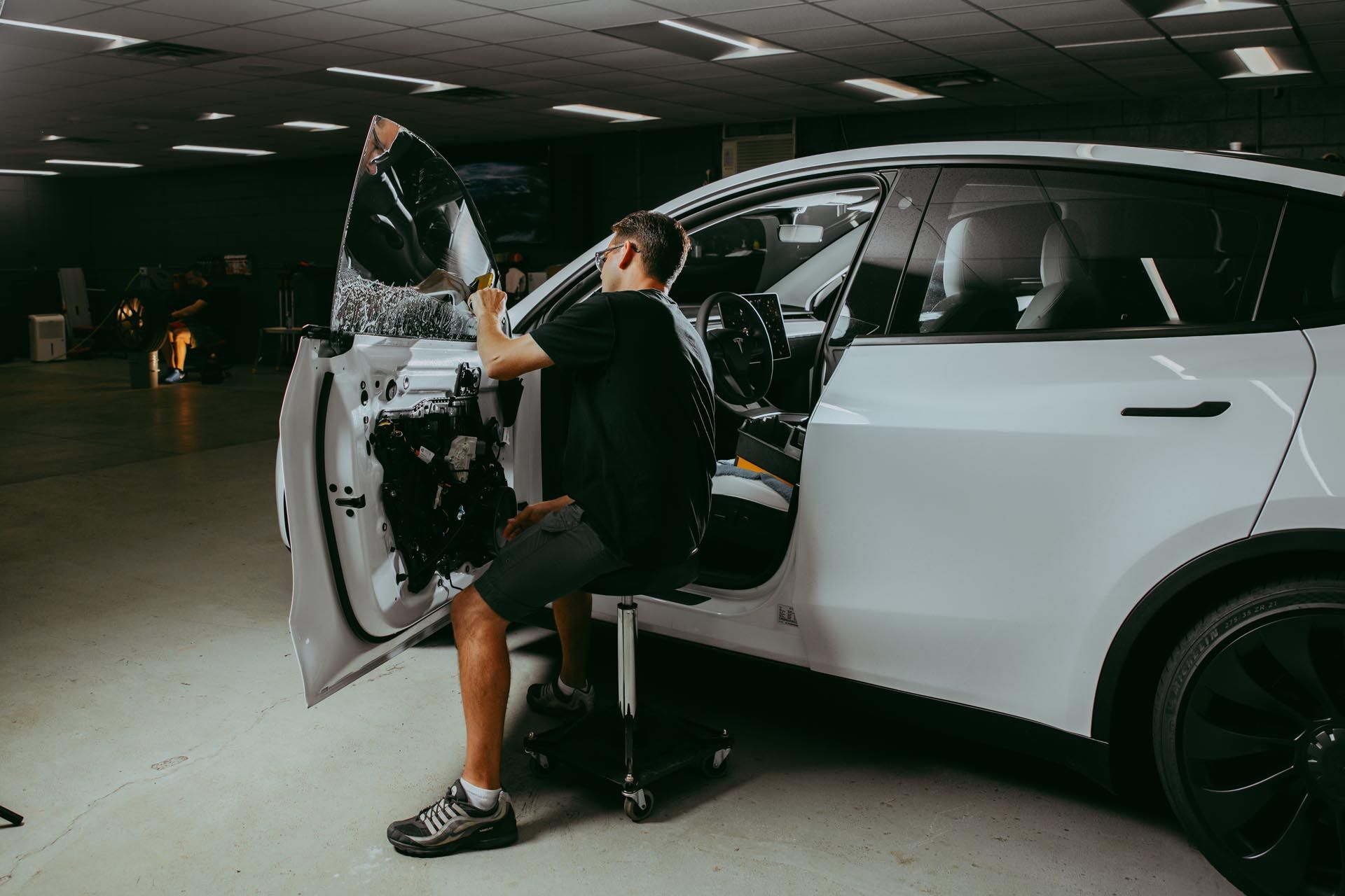 Person repairing the open door of a white car in a parking garage