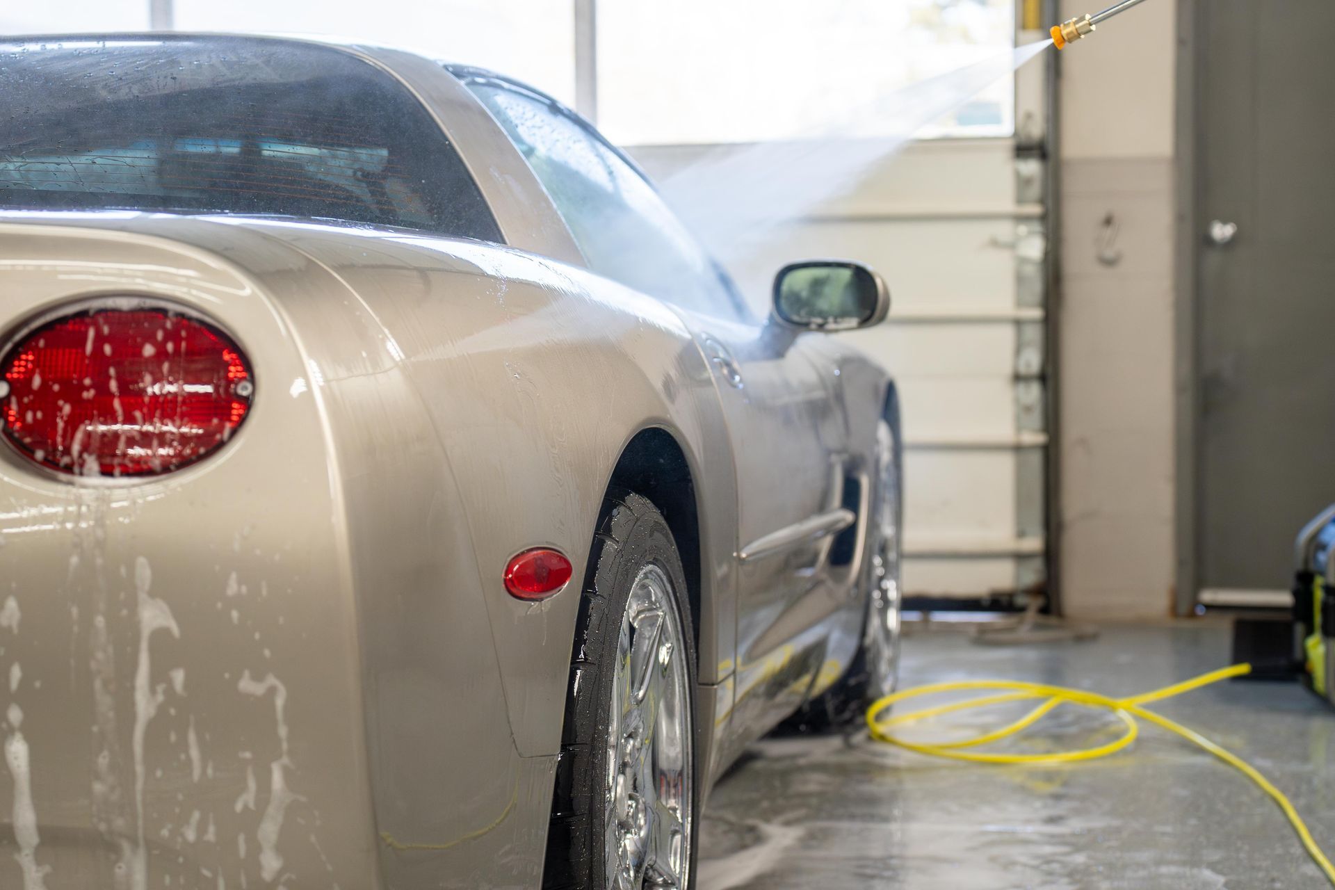 A car is being washed with a high pressure washer in a garage.