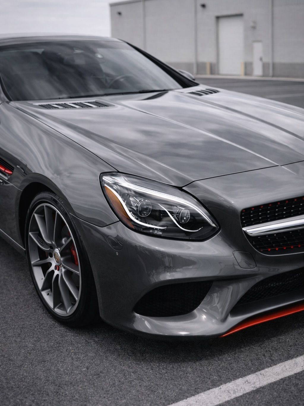 A gray Mercedes-Benz sports car parked in a paved lot, featuring a distinctive orange accent on the front bumper.