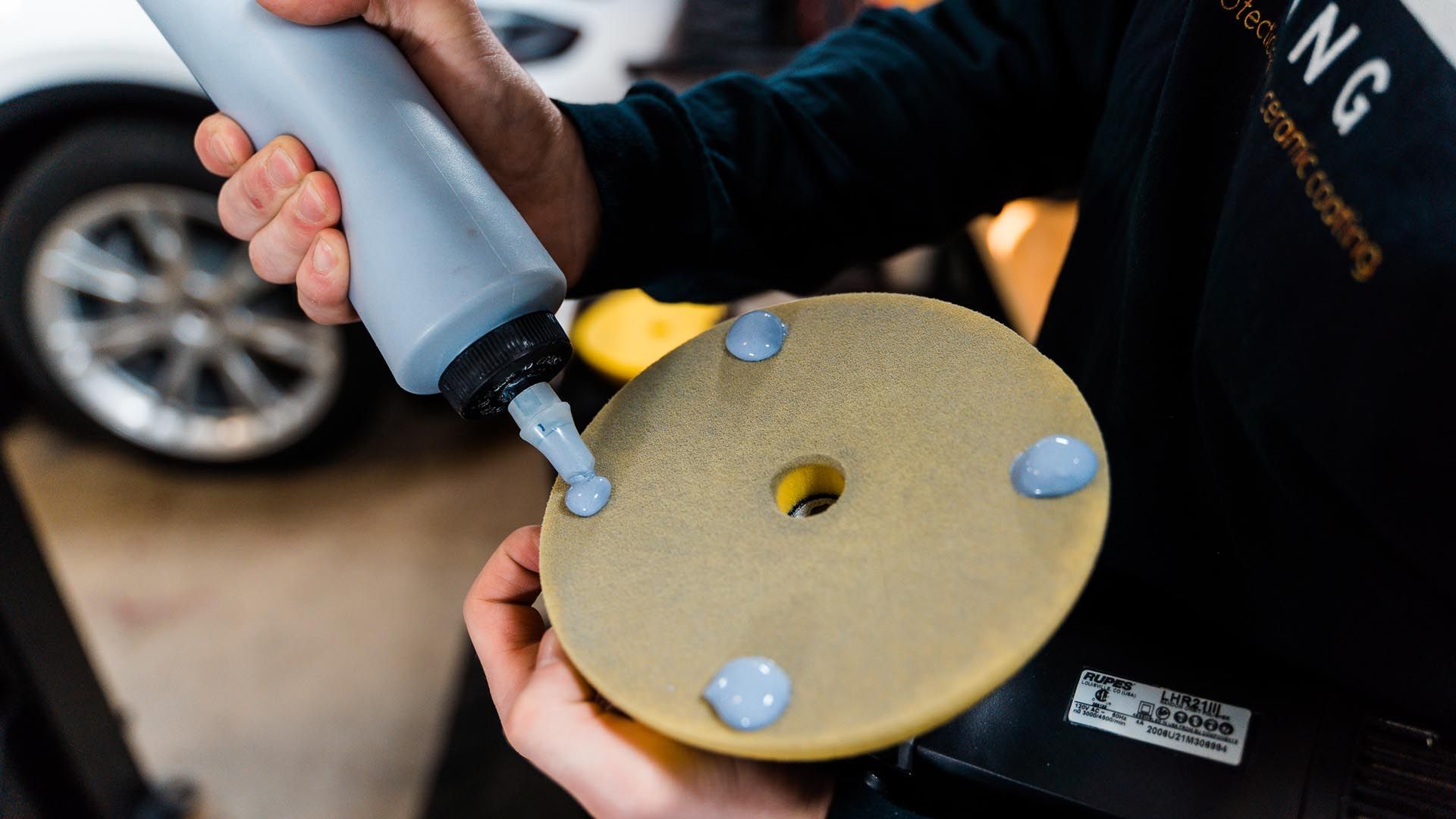 A person is holding a bottle of polish and a polishing pad.