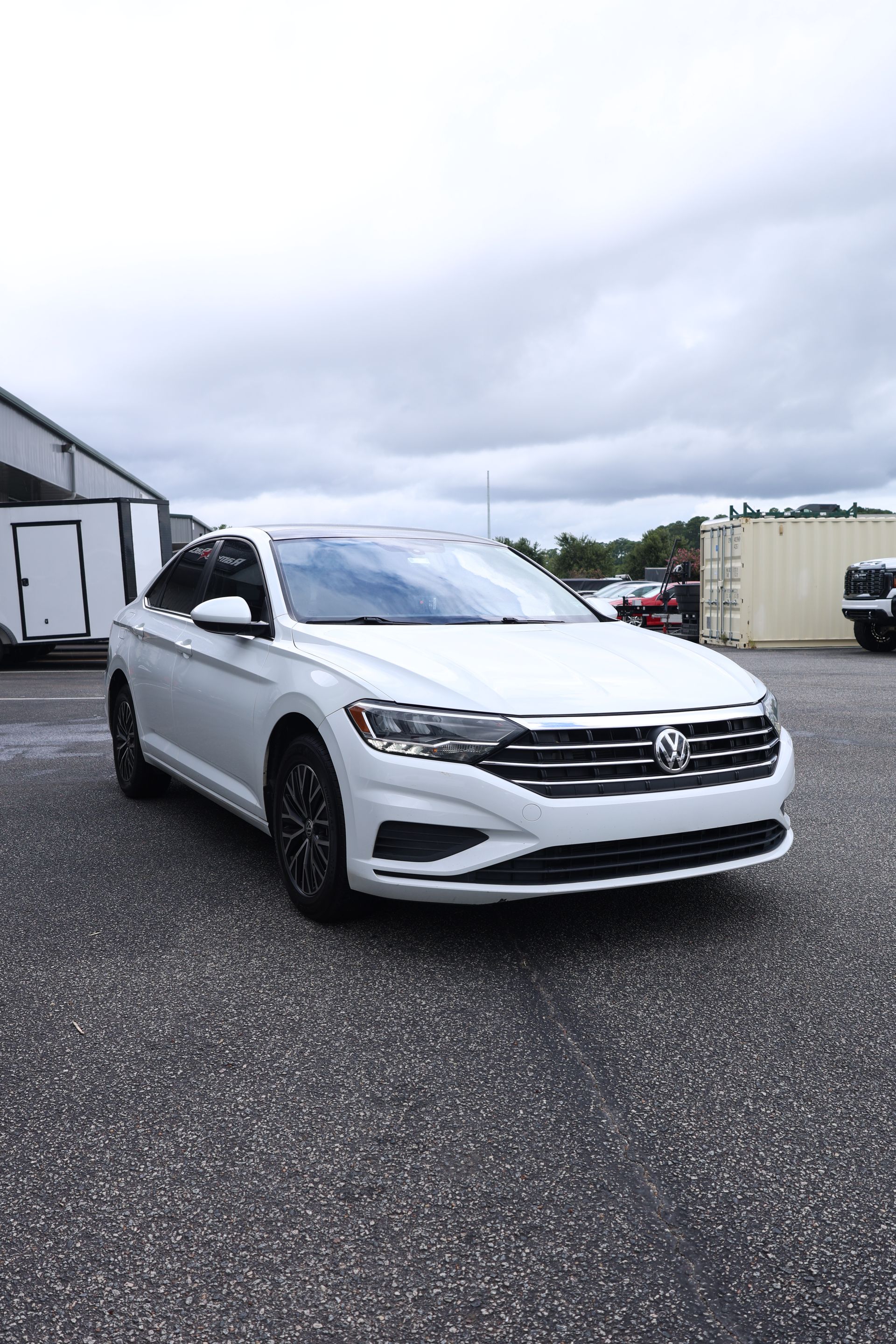 White Volkswagen Jetta parked on asphalt with cloudy sky in the background.