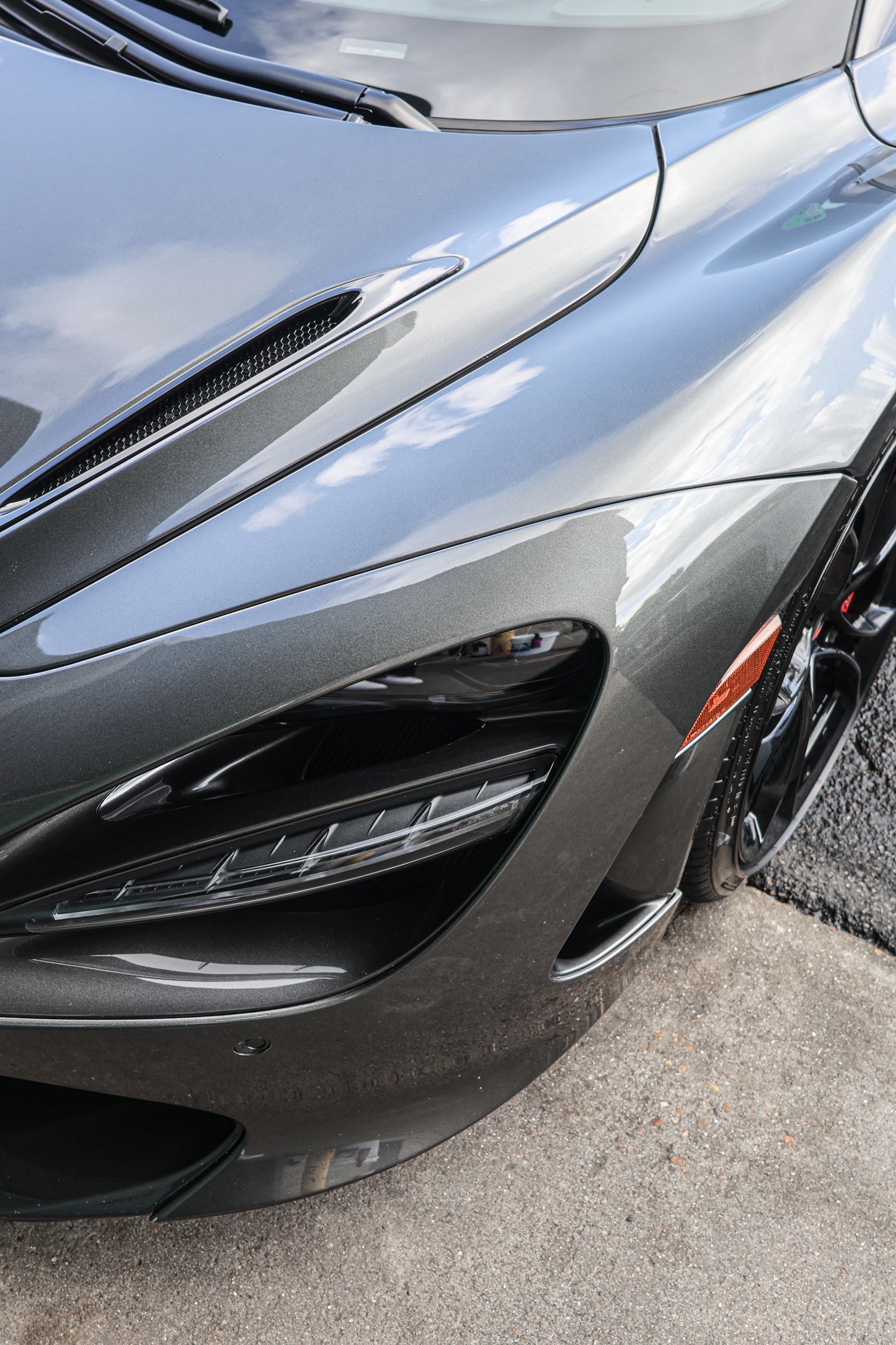 Gray McLaren sports car, close-up of headlight and front fender.