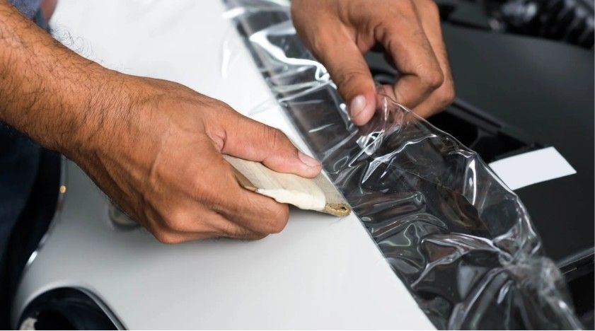 Person cutting film on a white car with a blade.