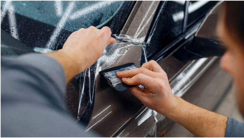 Hands applying film to a car window with a squeegee.