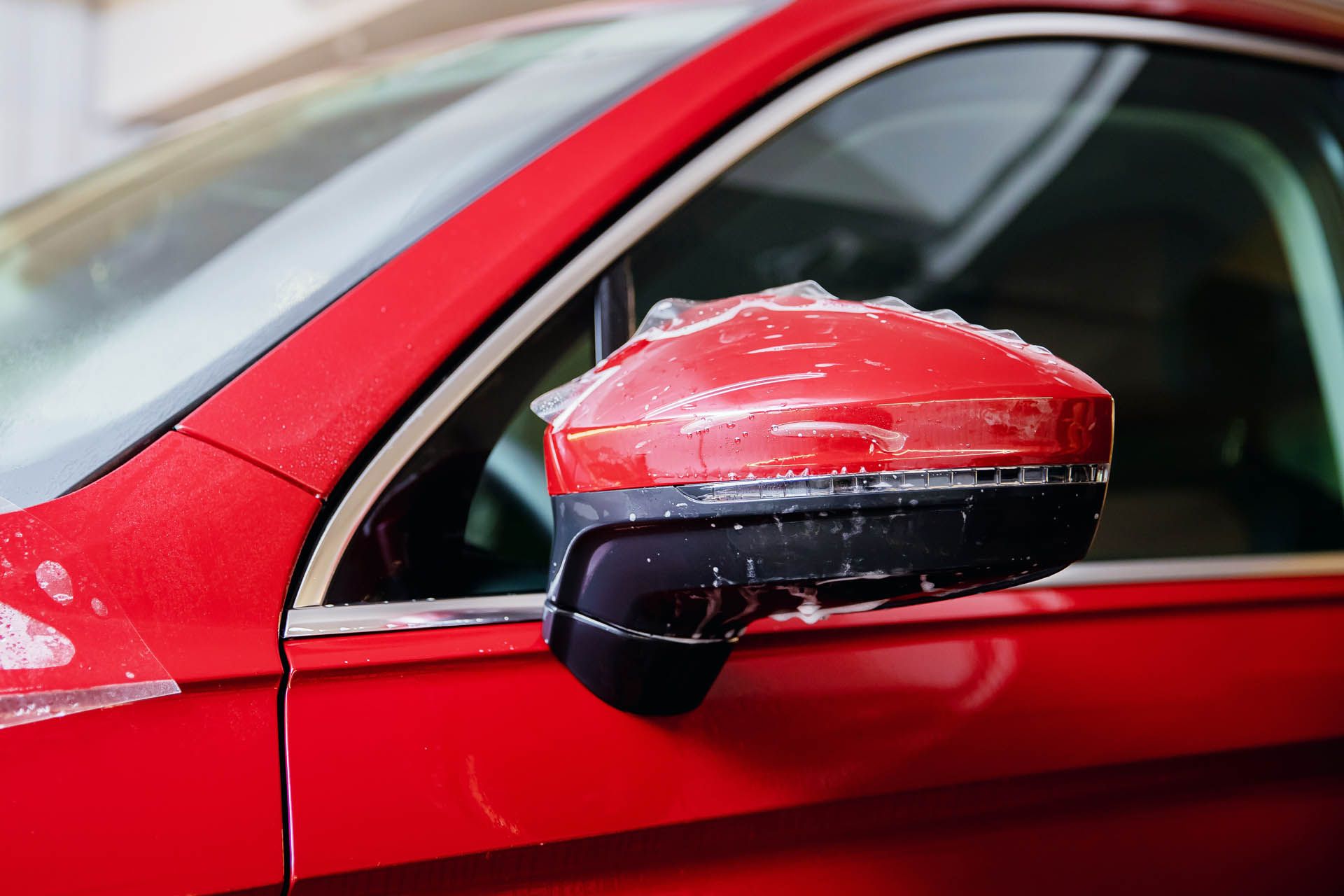 A close up of a red car with a rear view mirror wrapped in plastic.