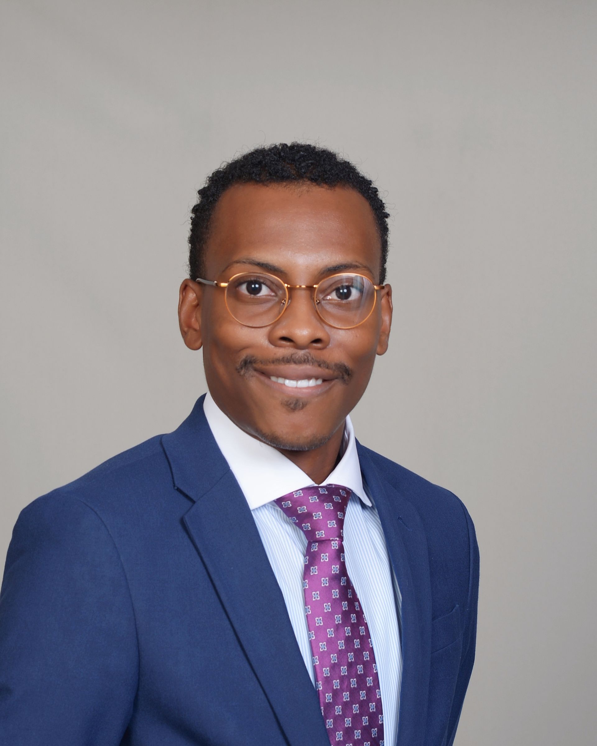 A man in a suit and purple shirt is smiling for the camera.