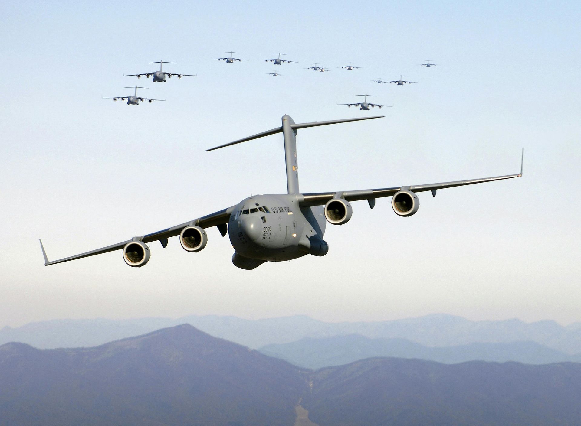 A large military plane is flying over a mountain range