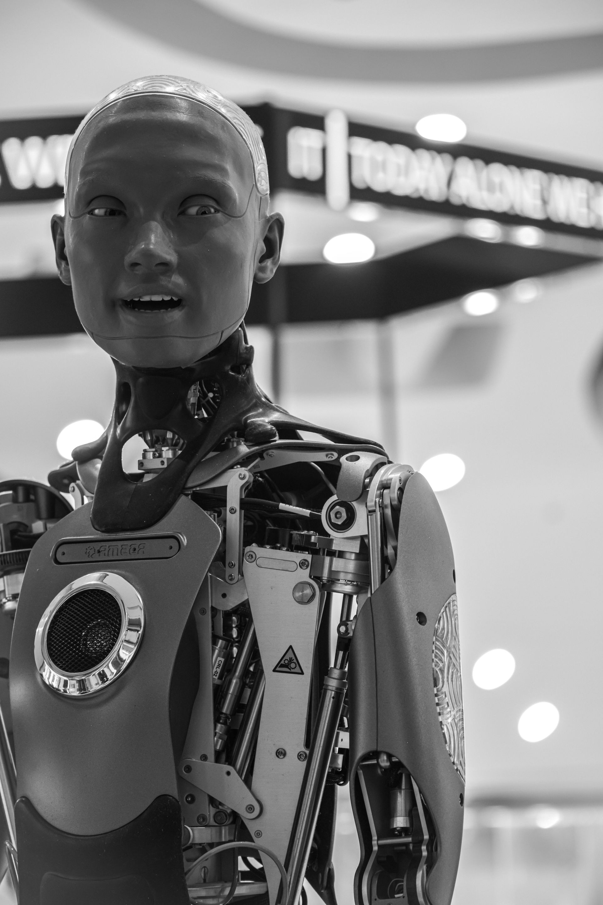 Humanoid robot with patterned body stands in a showroom, facing forward under bright lights.
