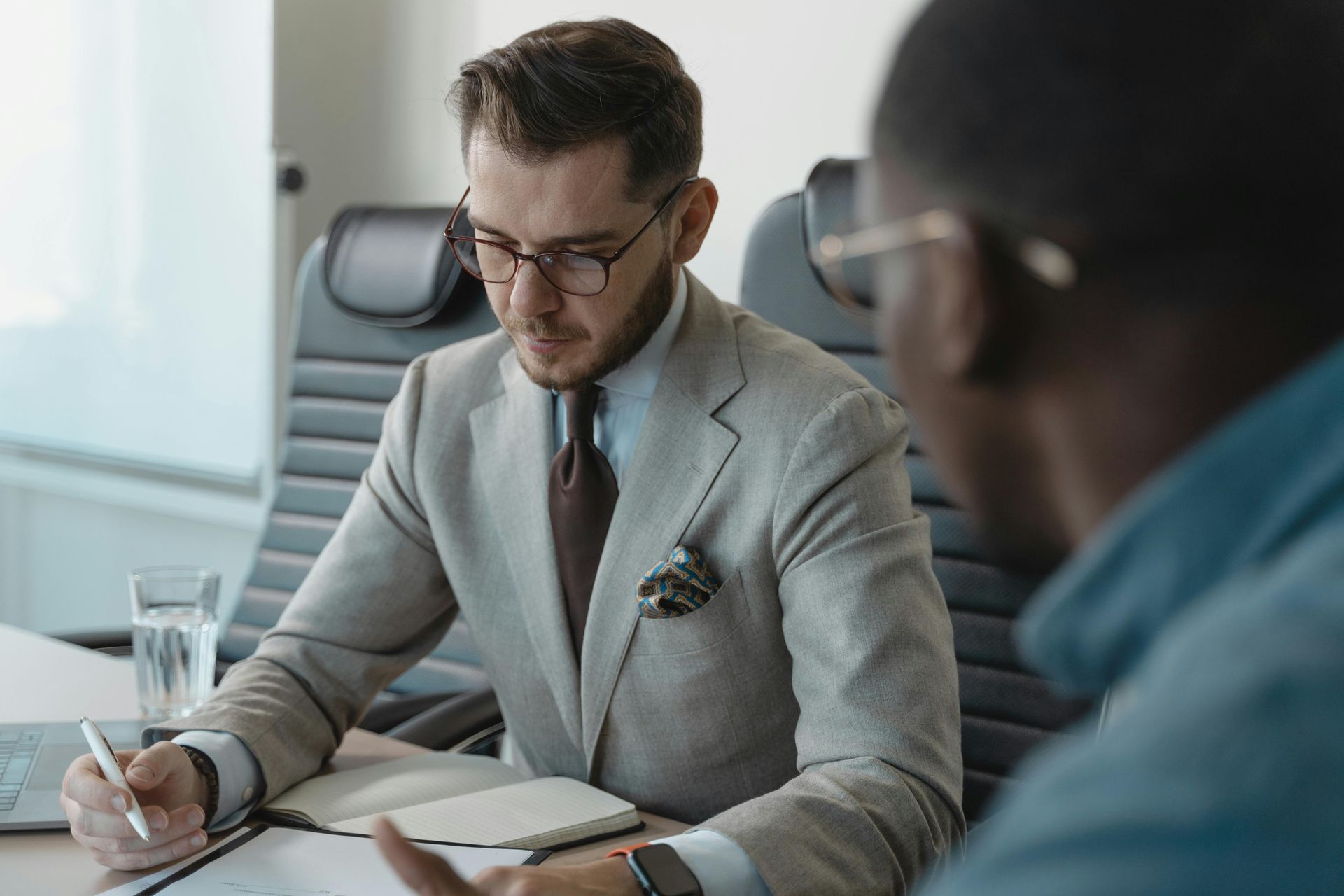 A man in a suit and tie is sitting at a table talking to another man.