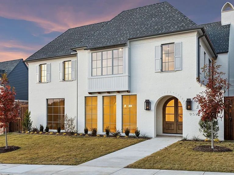 White two-story house with gray roof, brown door, arched entry, and large windows.