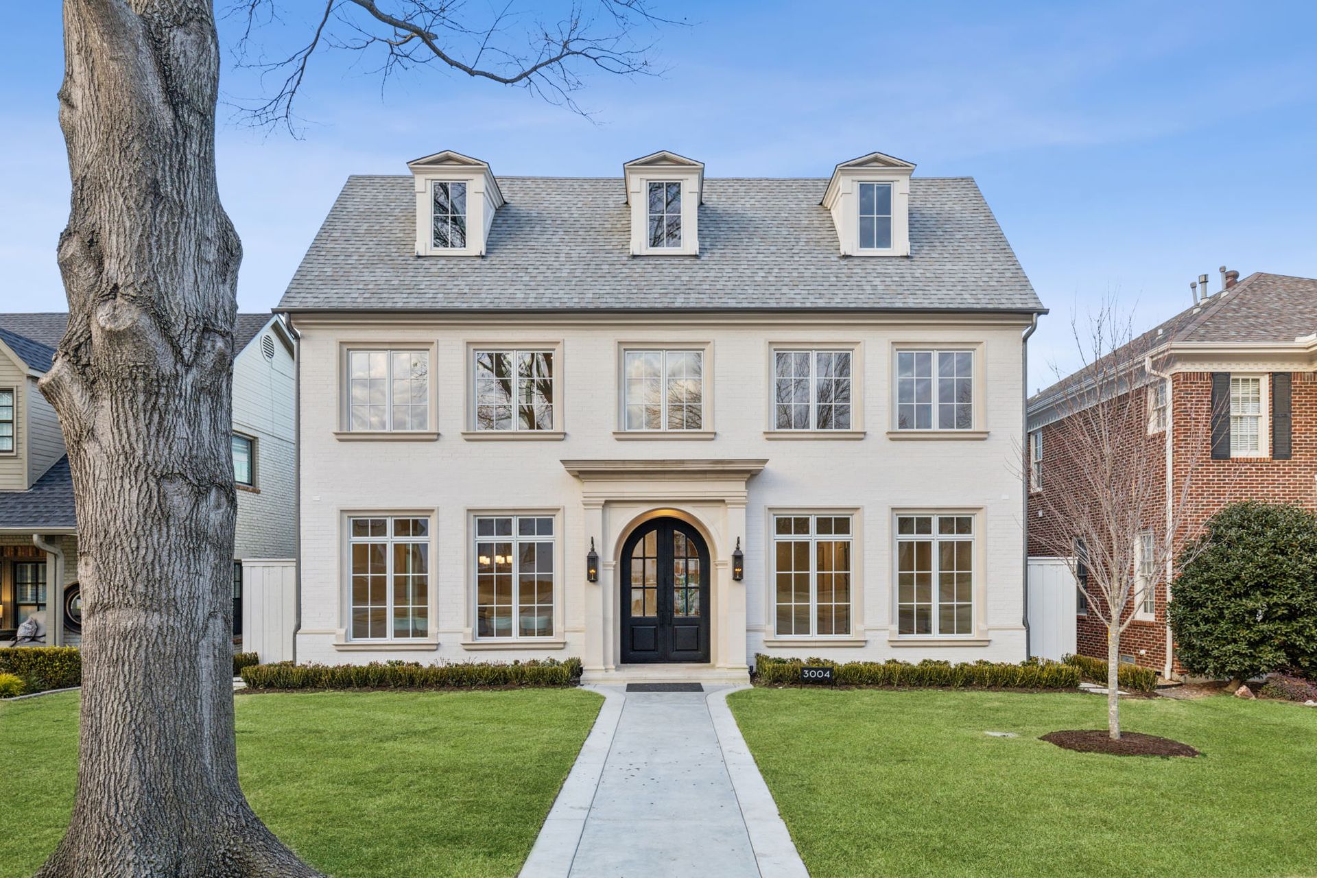 White stucco house with gray tile roof, three dormers, green lawn, and a walkway.