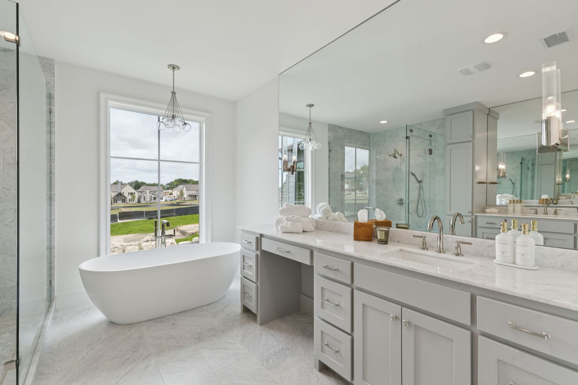 Bright white bathroom with a free-standing tub, large mirror, and vanity with a window view.