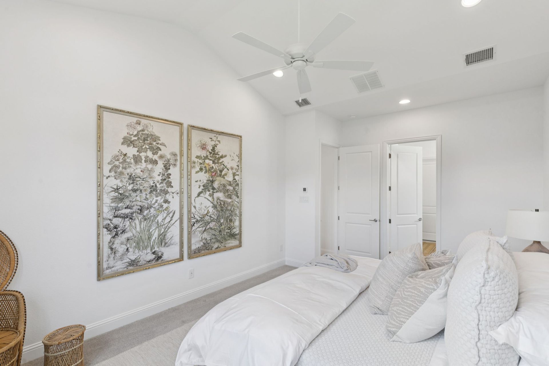 Bedroom with white walls, bed, and art prints; a ceiling fan hangs above.