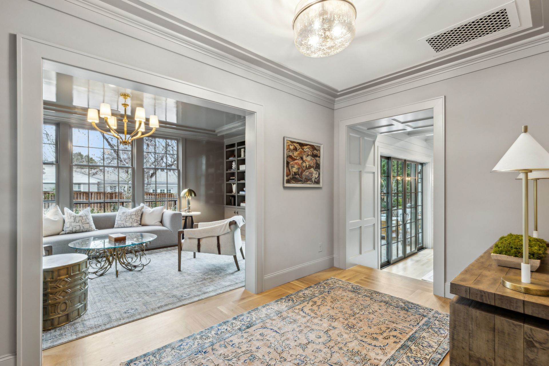 A gray entryway with doorways to a living room with windows, and a sunroom.