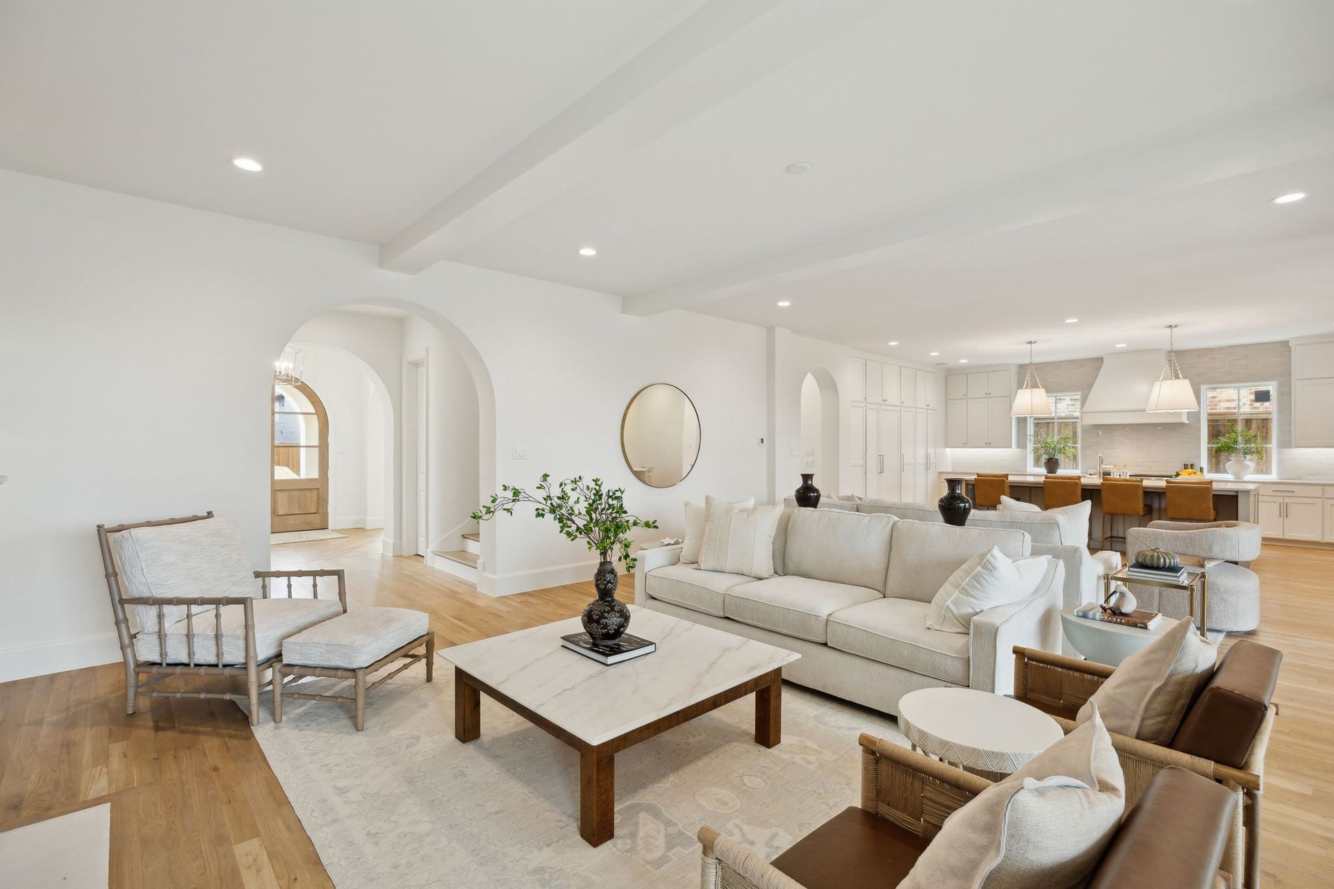 Bright, open living room with a white couch, chairs, and a view of the kitchen.