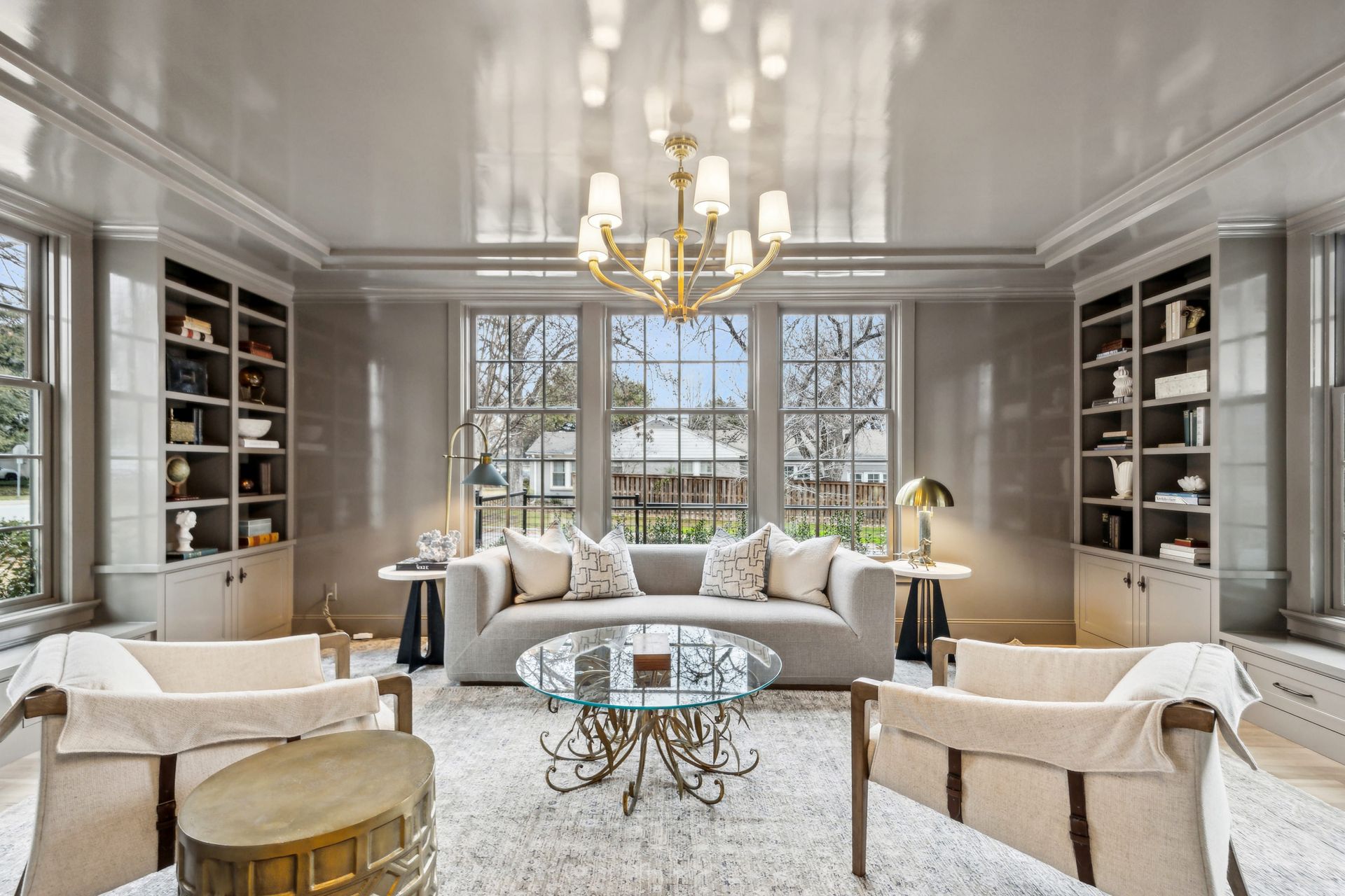 Living room with a gray sofa, chairs, bookshelves, windows, and a chandelier.