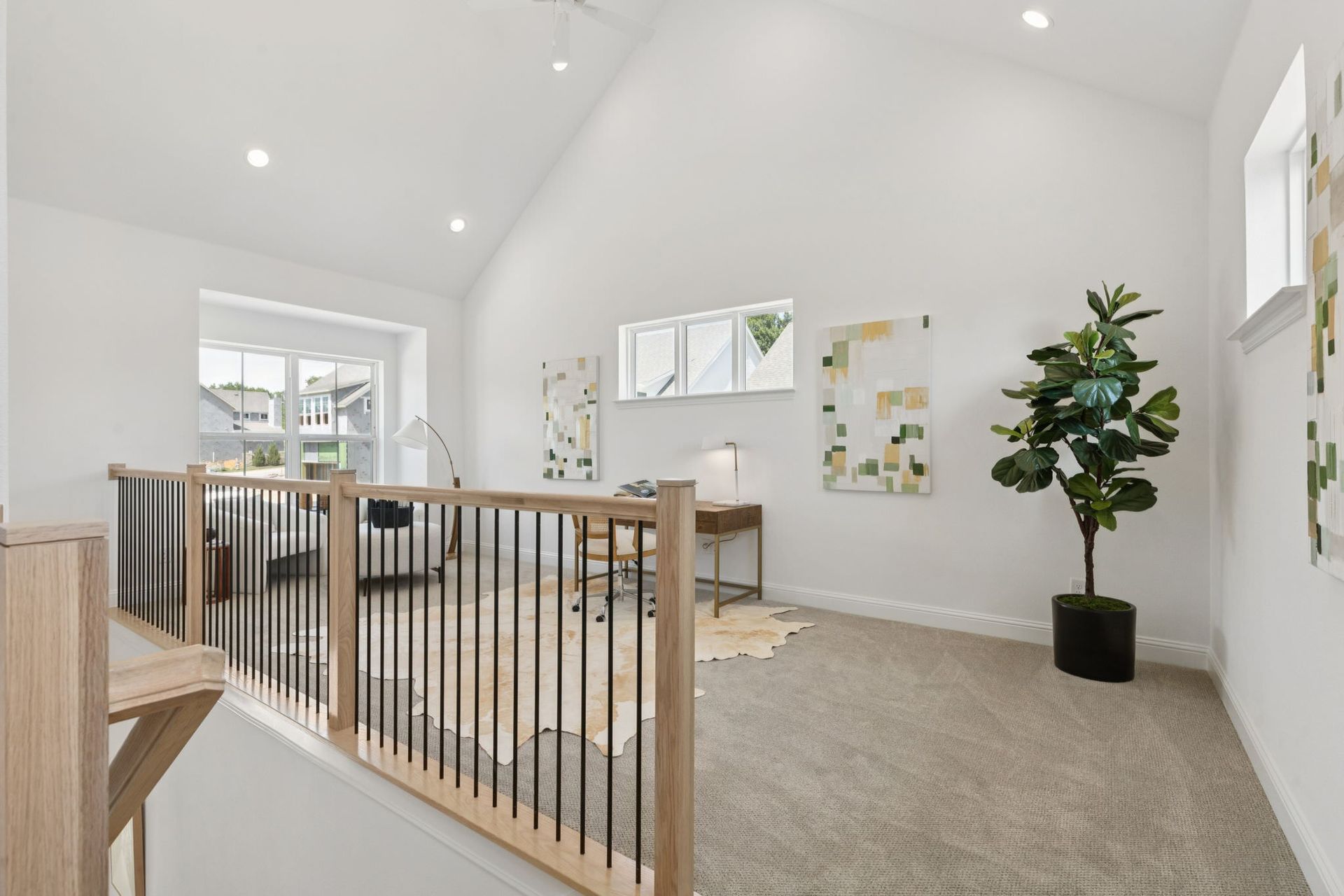 Loft with a light wood railing, desk, art, a large plant, and white walls.