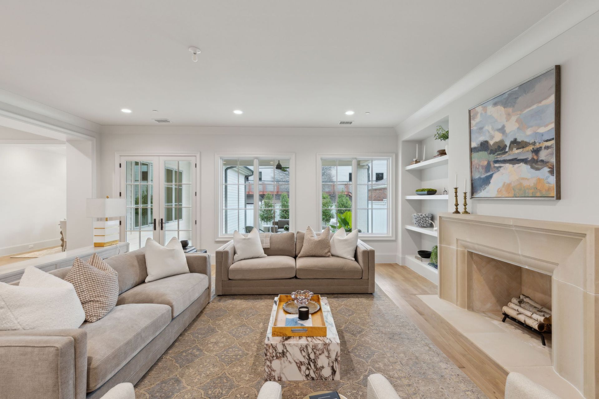 Living room with light-colored couches, fireplace, and windows. Neutral tones, hardwood floors, and modern decor.