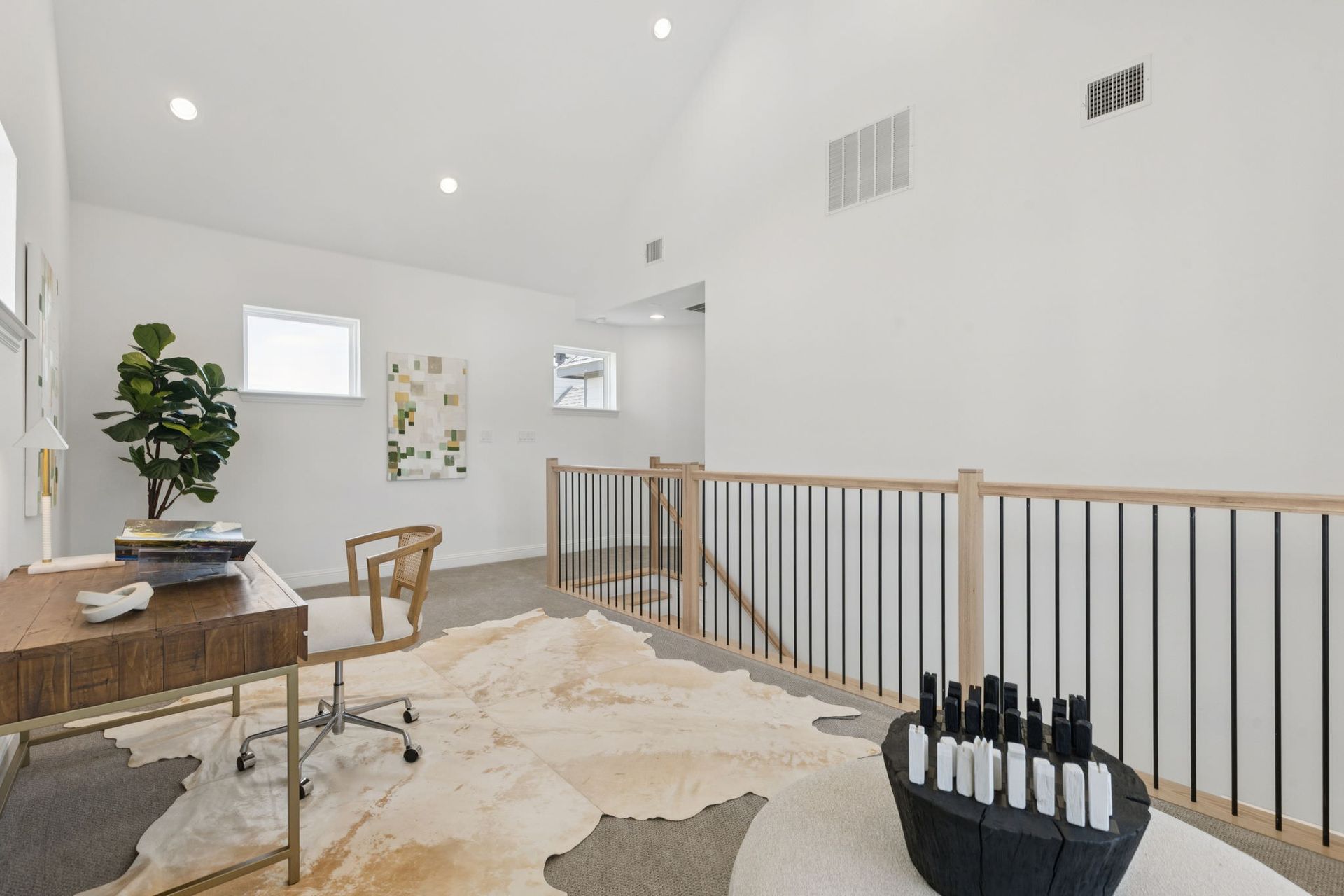 Home office with desk, plant, rug, and railing. White walls and high ceiling.