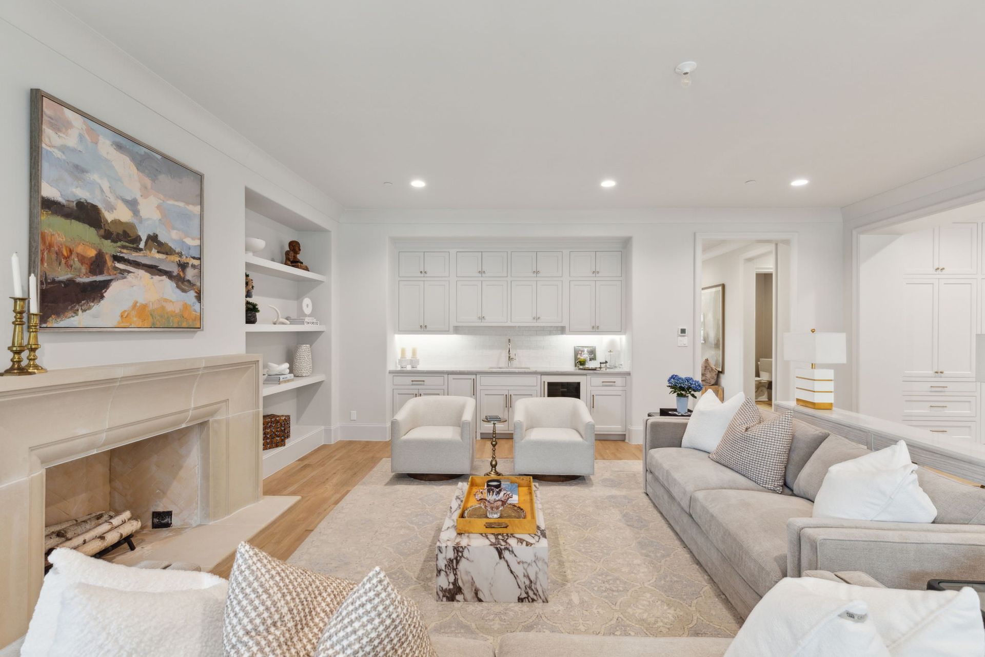 Living room with fireplace, built-in shelving, and small kitchen area; neutral color palette.