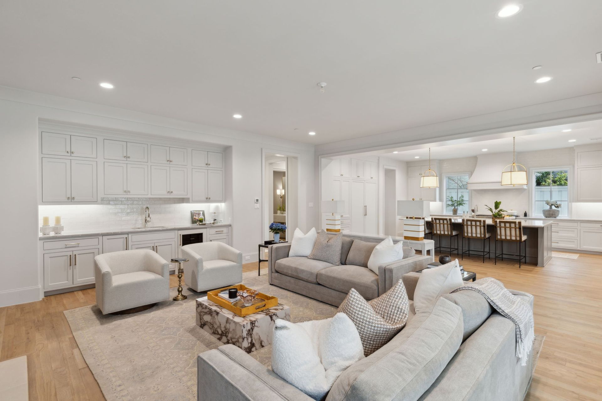 Bright, modern living room with open kitchen. Gray sofas, white cabinets, light wood floors.