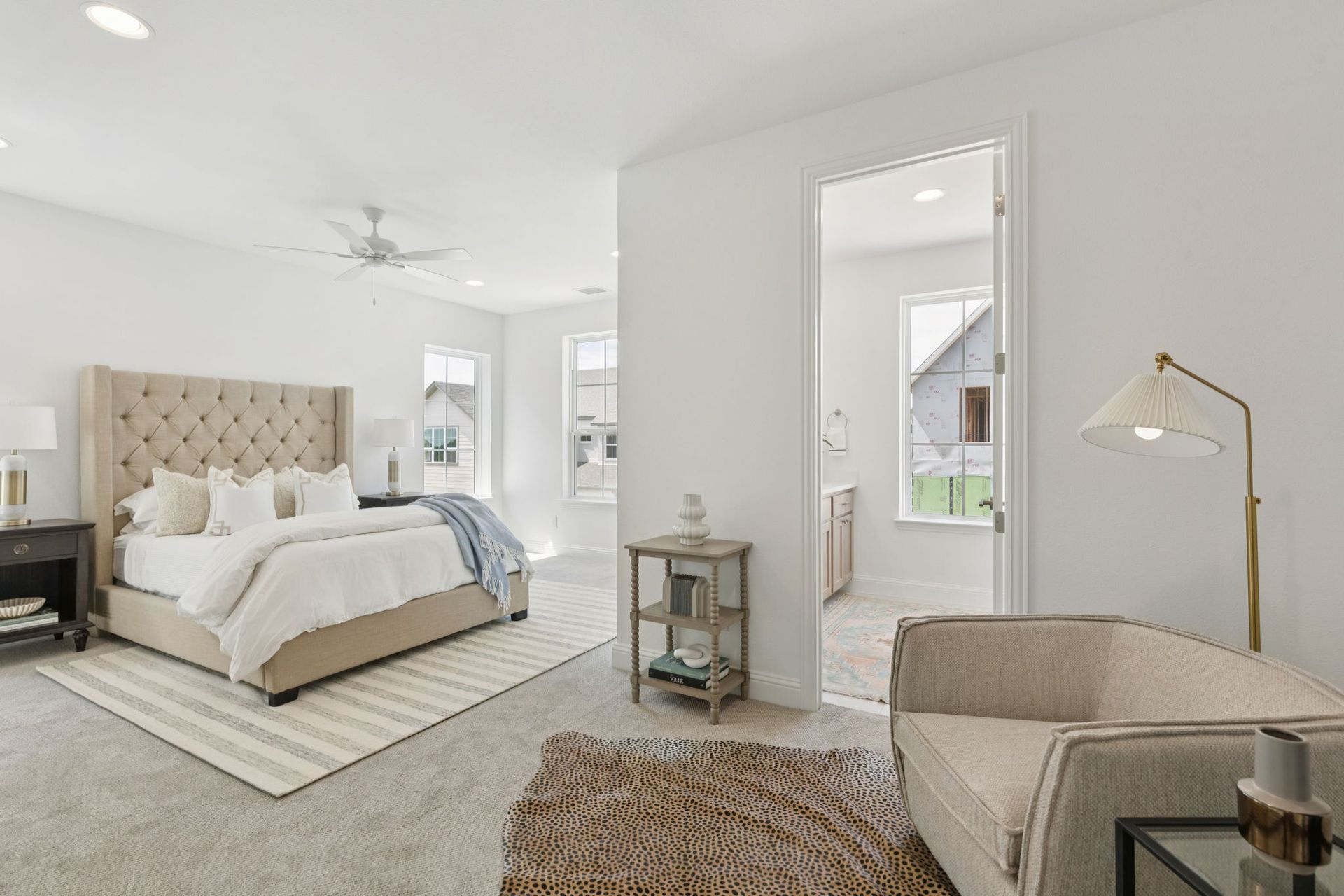 Spacious white bedroom with bed, armchair, rug, and doorway to bathroom.