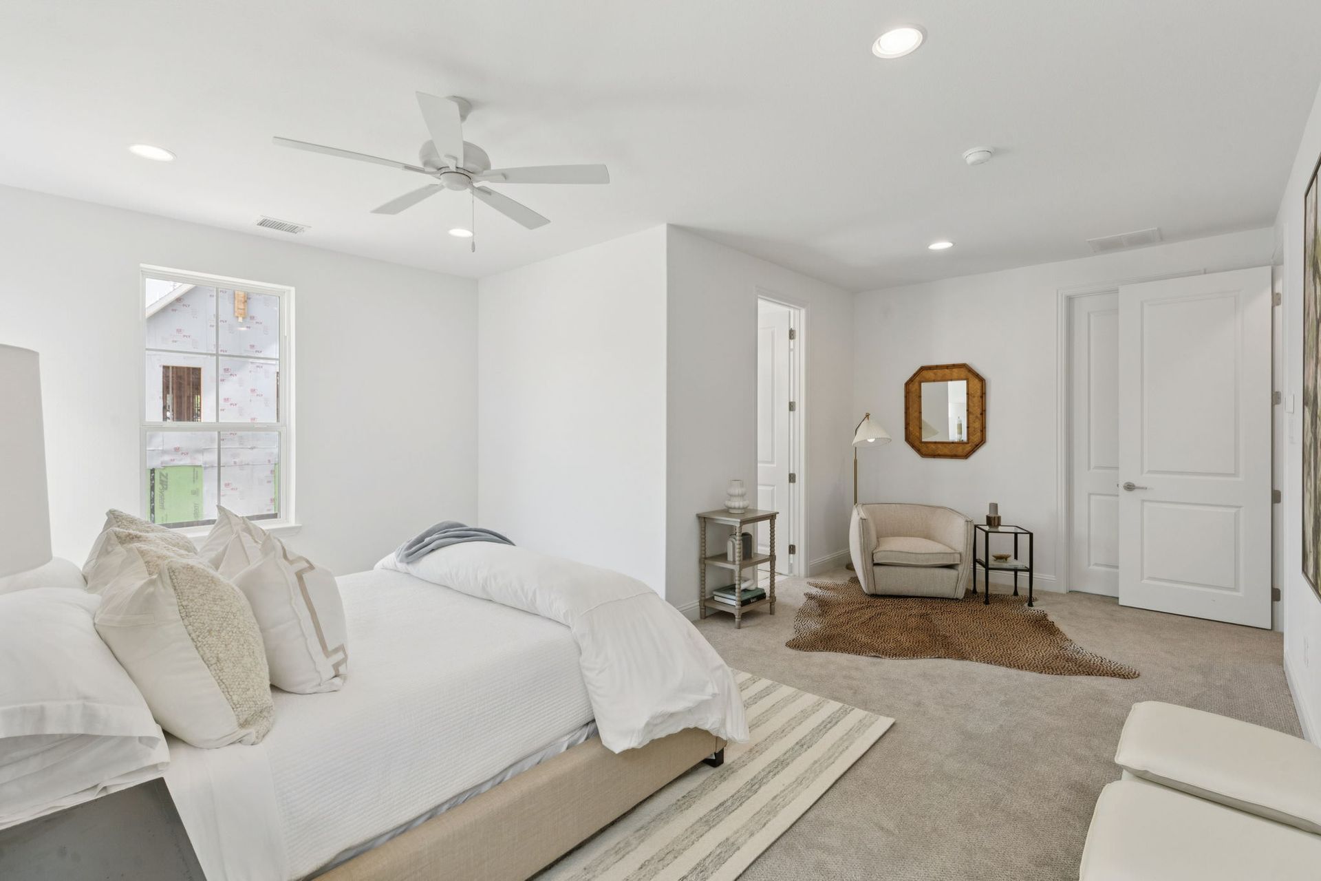 Bright bedroom with bed, chair, rug, window, and white walls.