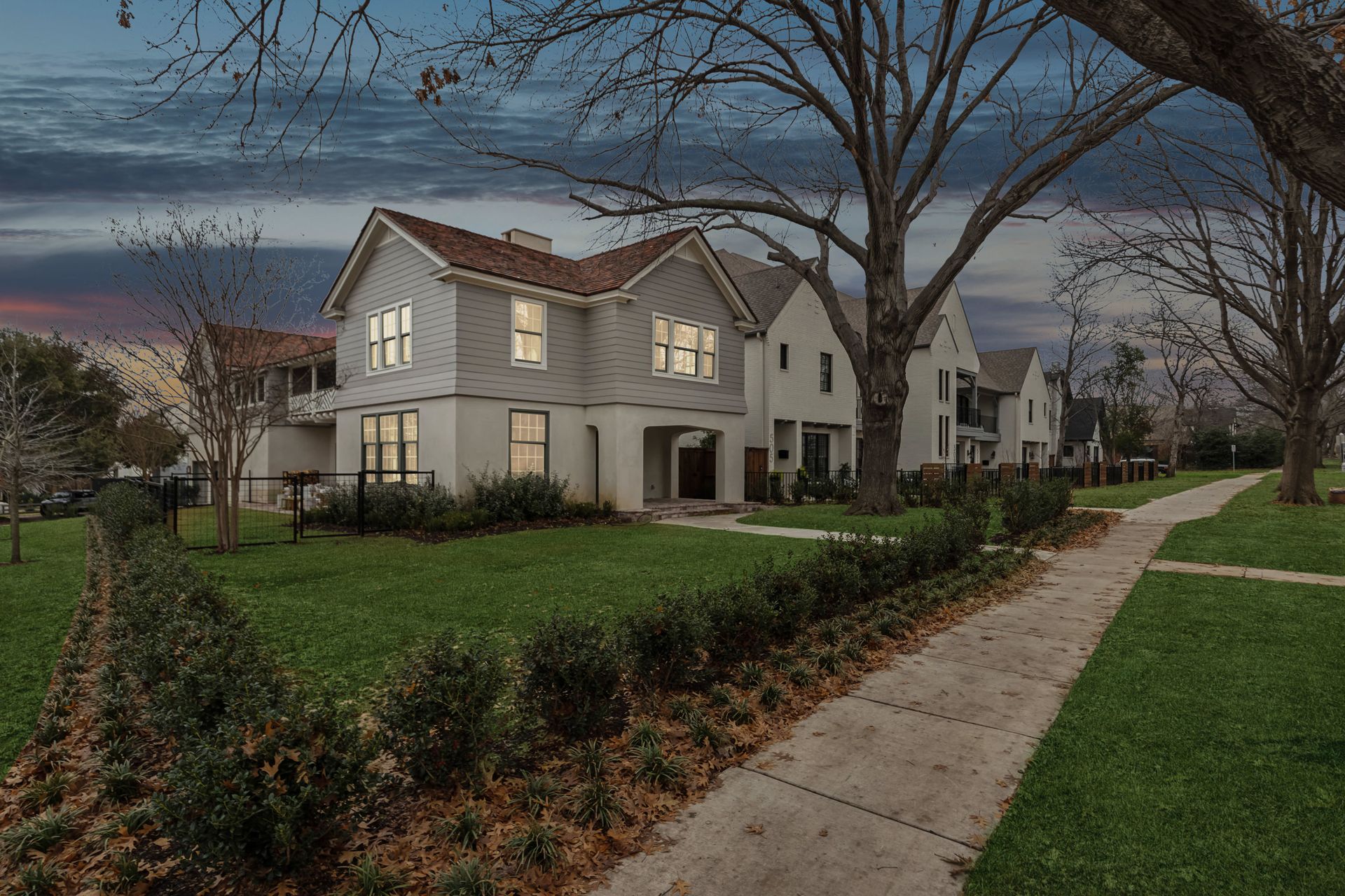 Two-story white house at dusk with a sidewalk, trees, and green lawn.